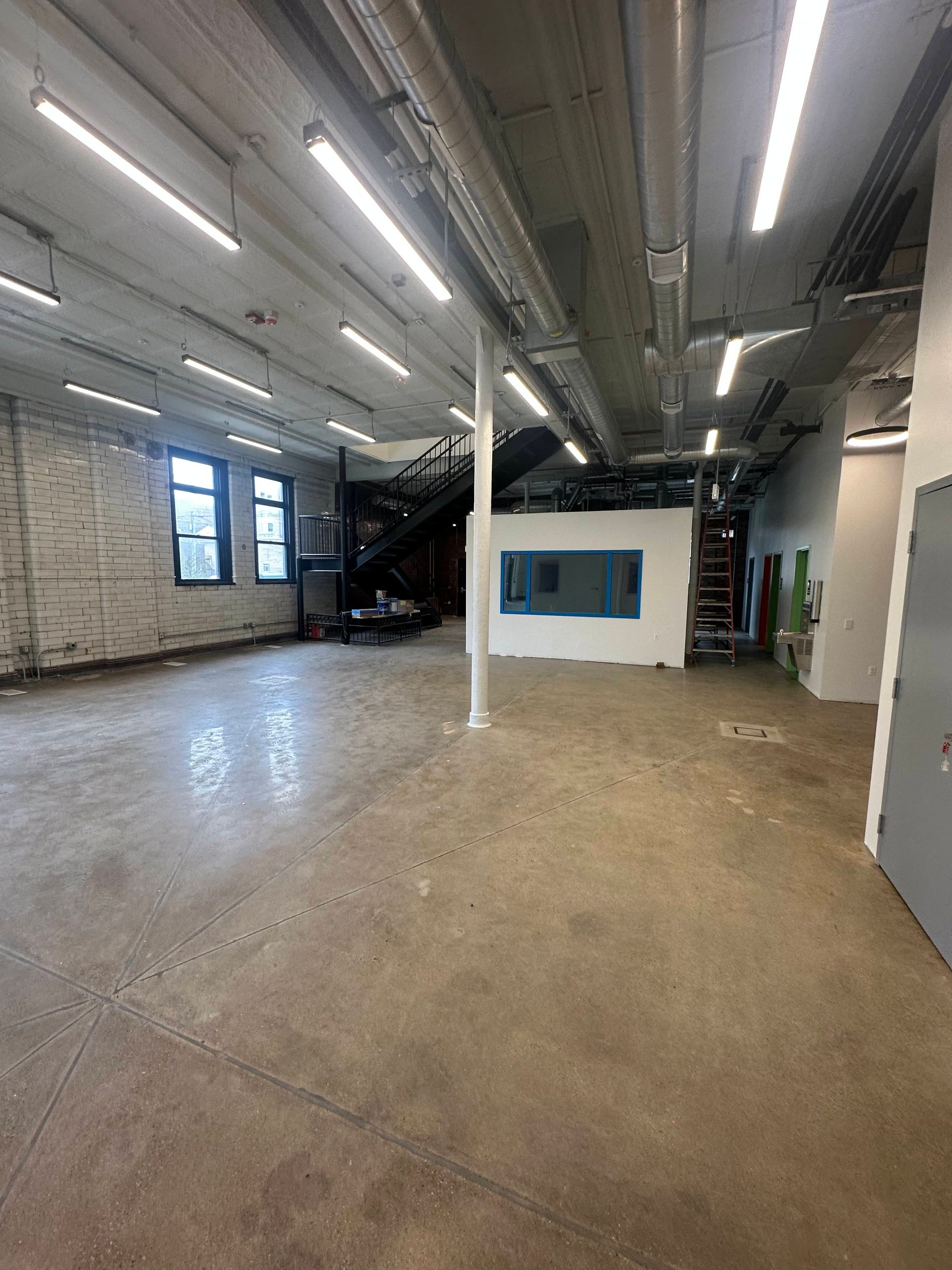 Empty industrial space with concrete floor, exposed pipes, and a central pillar.