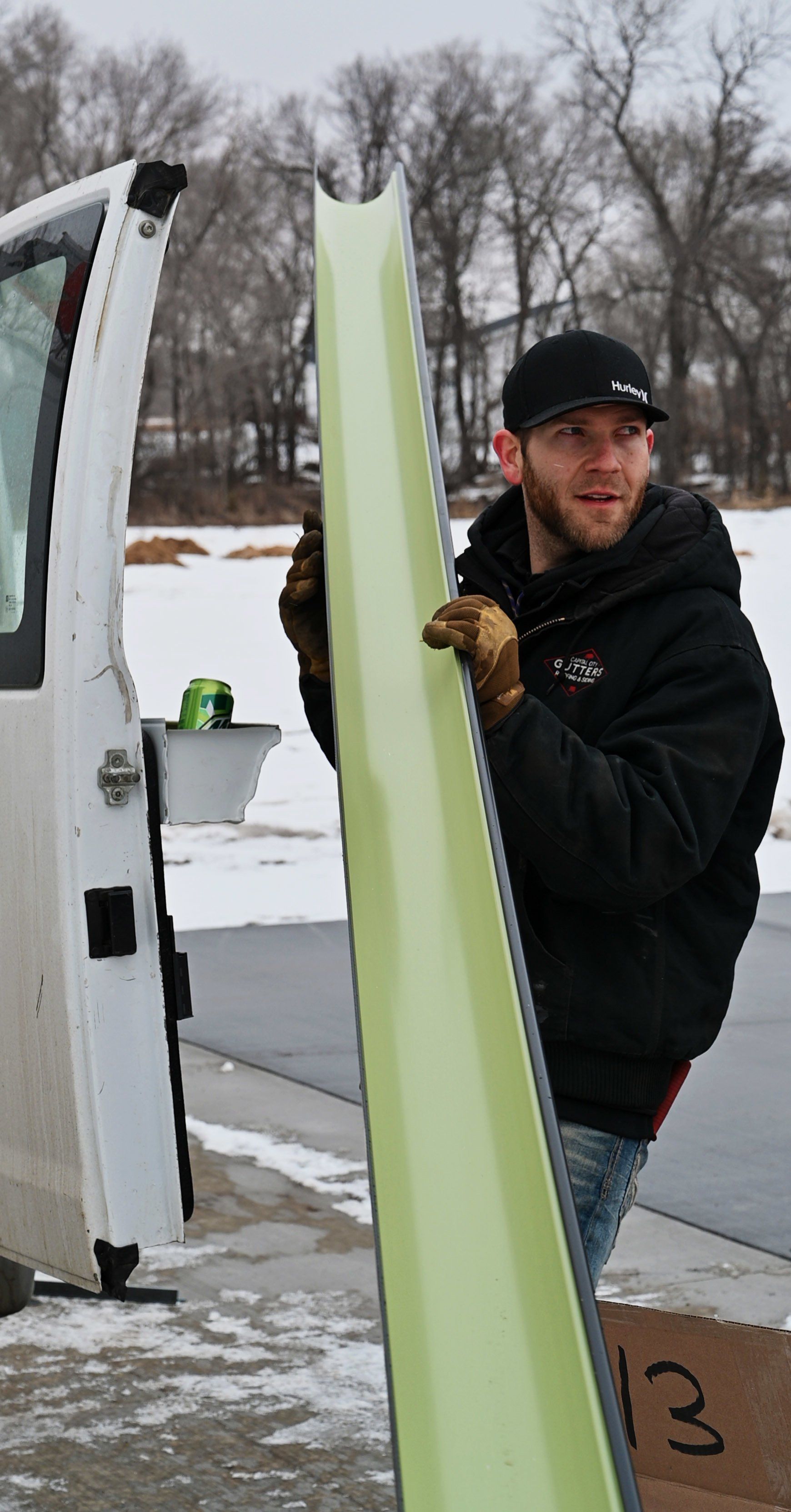 a man in a black jacket is carrying a yellow item out of a van .