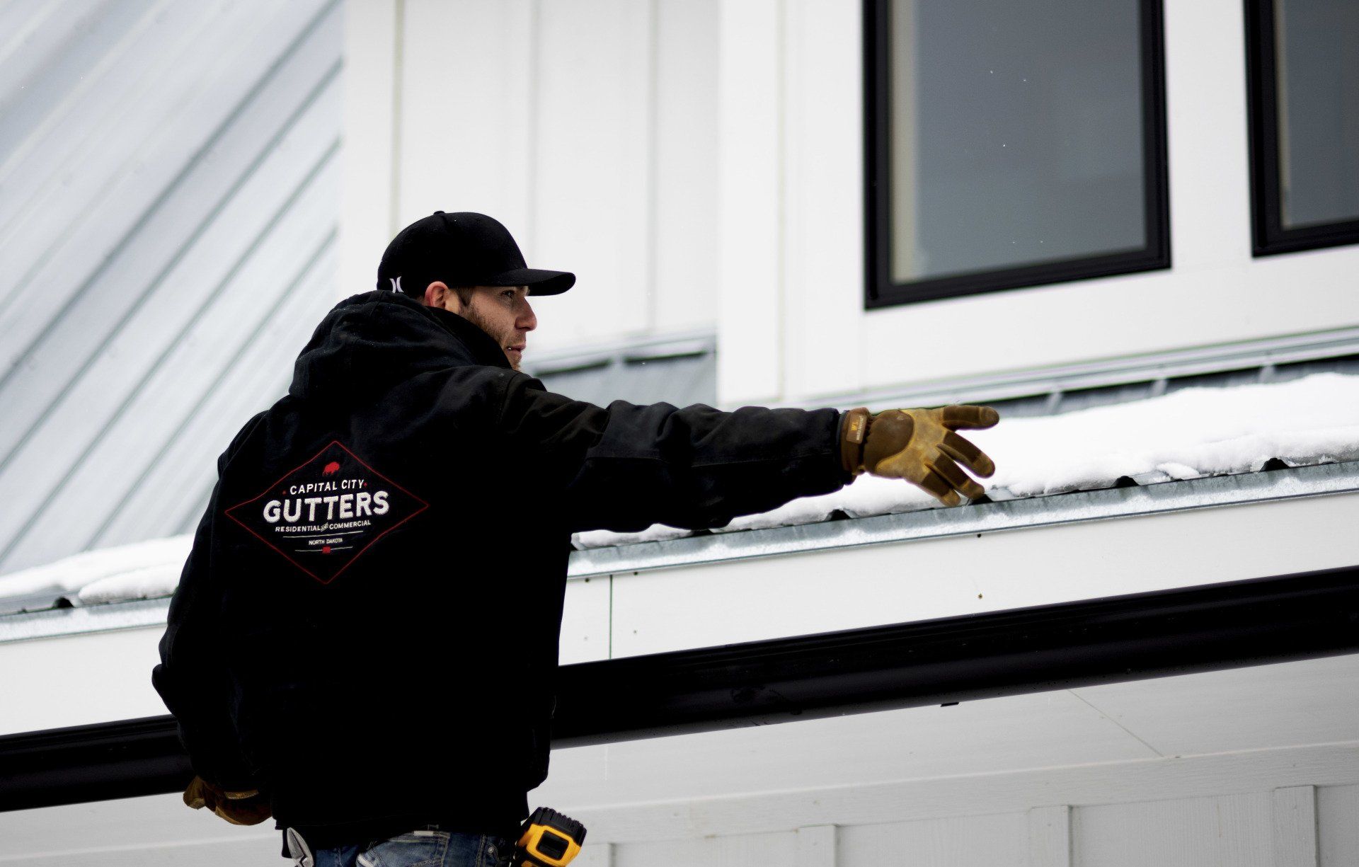 a man wearing a black jacket with the word gutters on the back is standing on a roof .