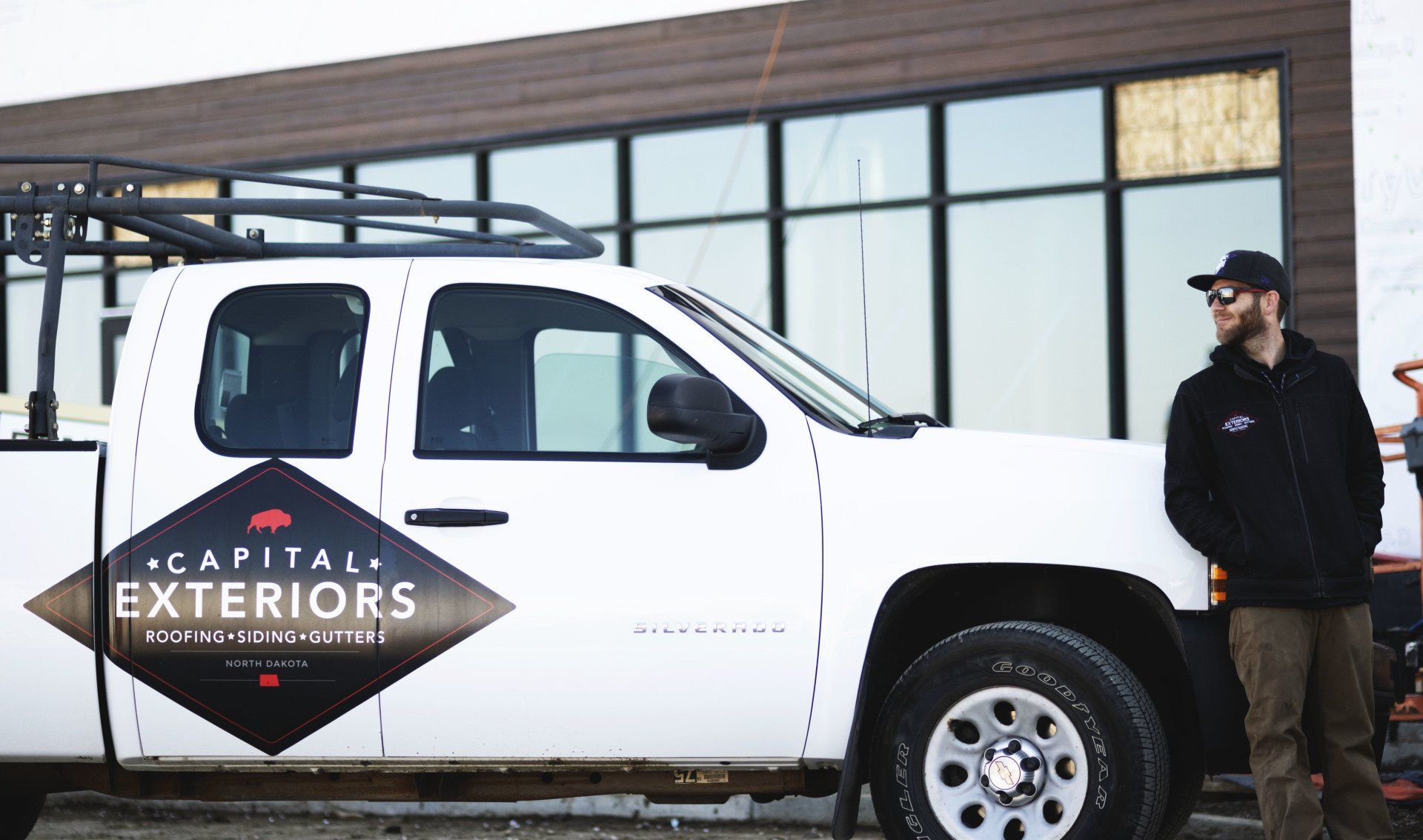 a man is standing next to a white truck that says capital exteriors .