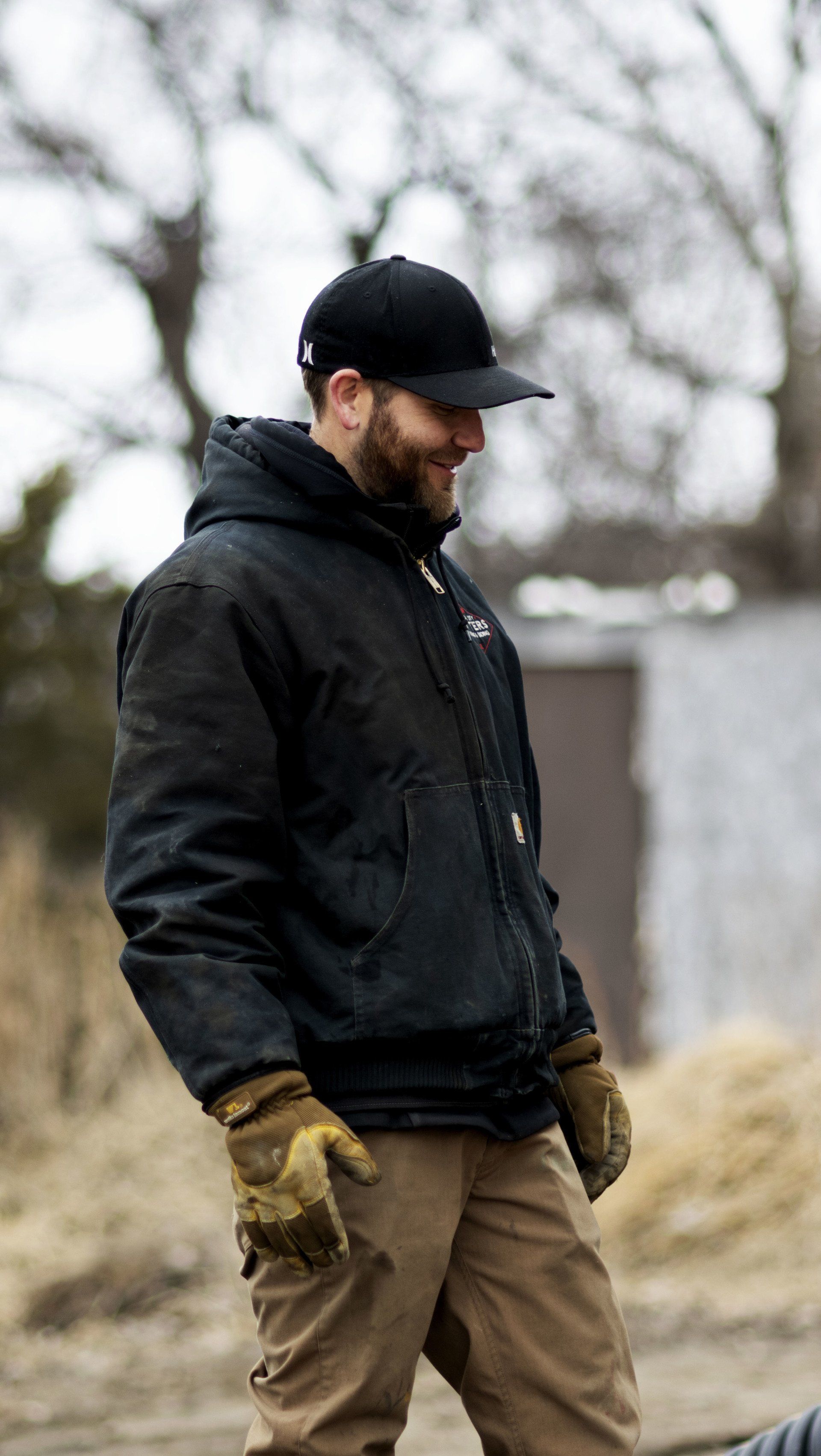 a man wearing a black jacket and a black hat is standing in the dirt .