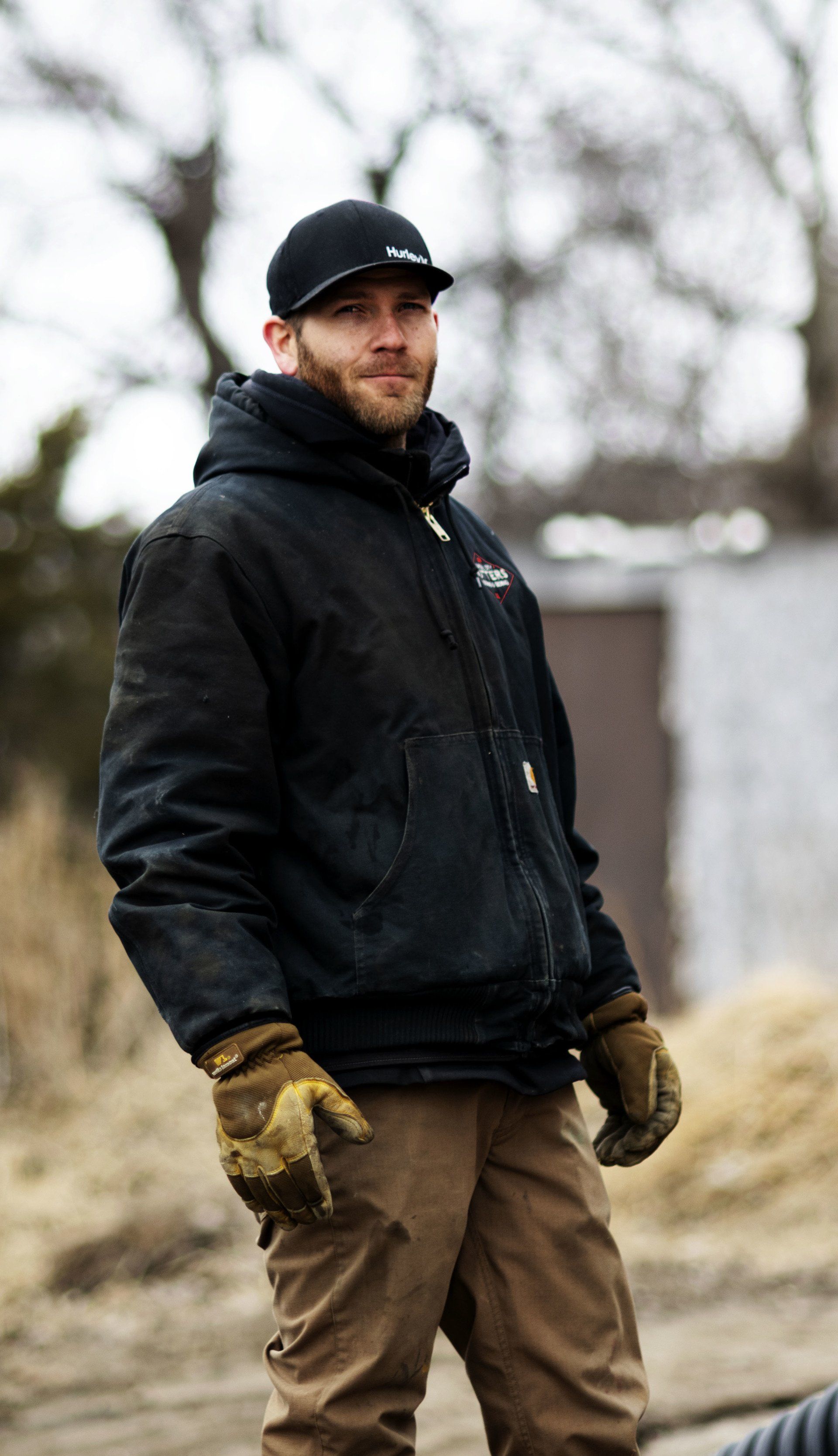 a man wearing a black jacket and a hat is standing in a field .
