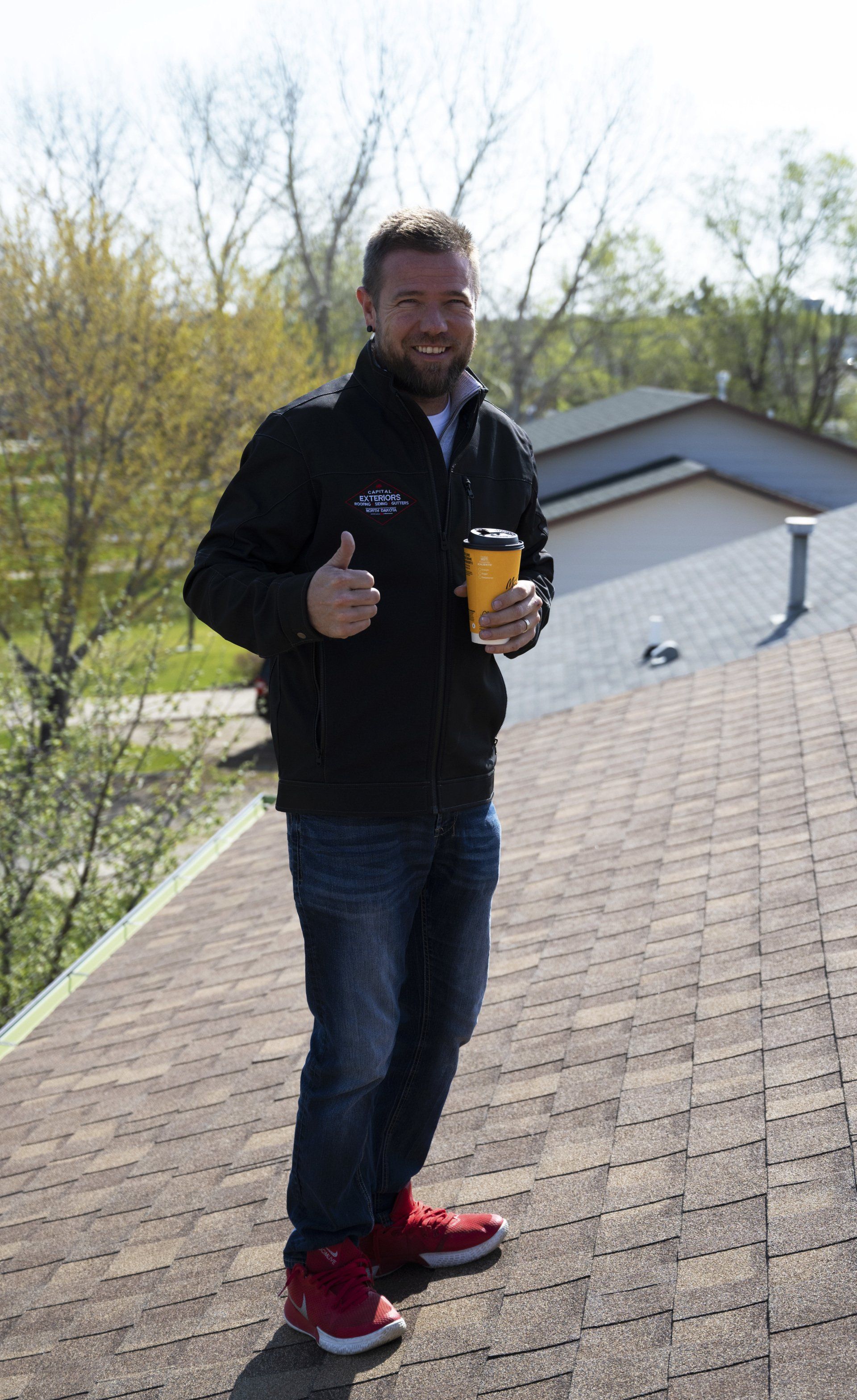 a man is standing on a roof holding a cup of coffee and giving a thumbs up .