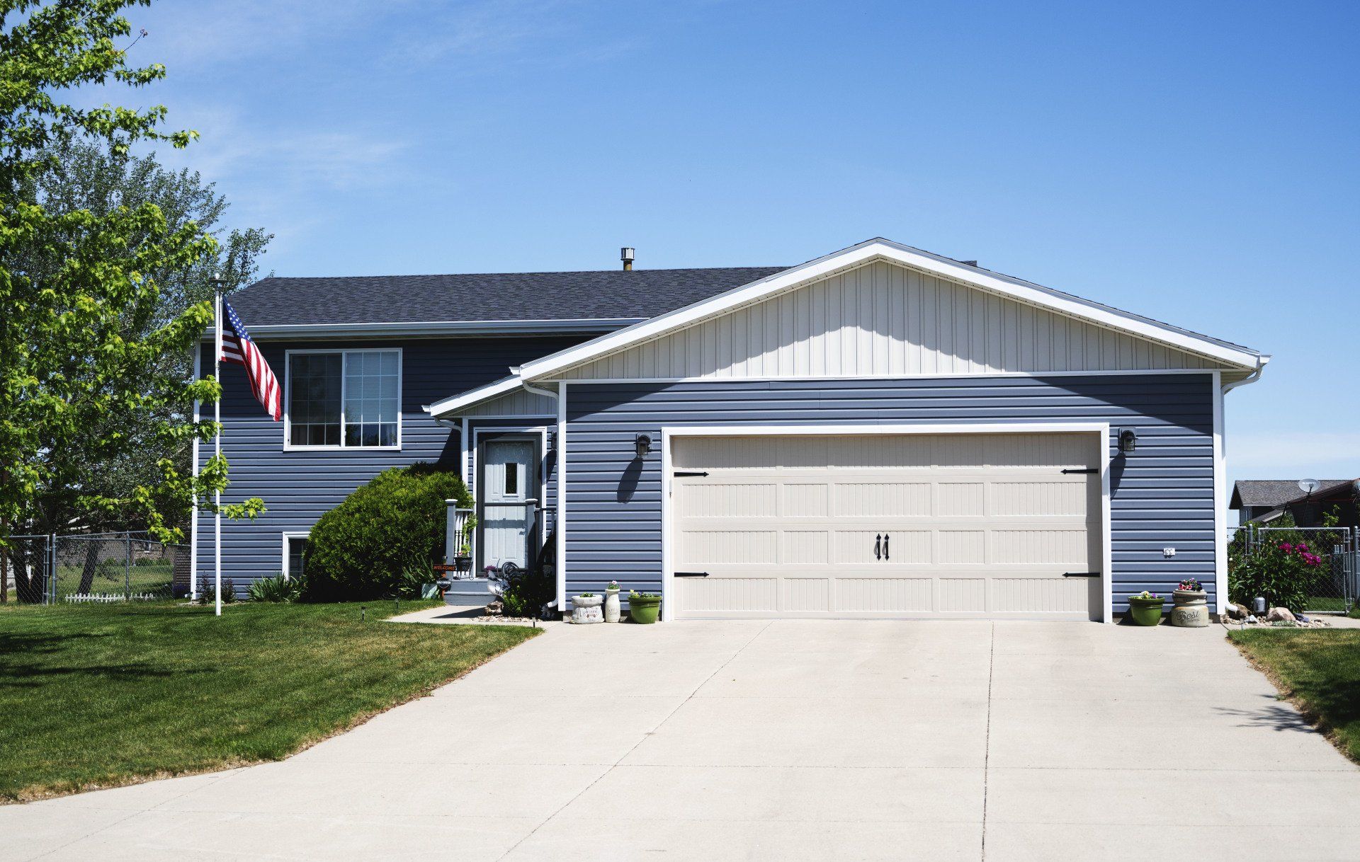a blue house with a white garage door and an american flag in front of it .