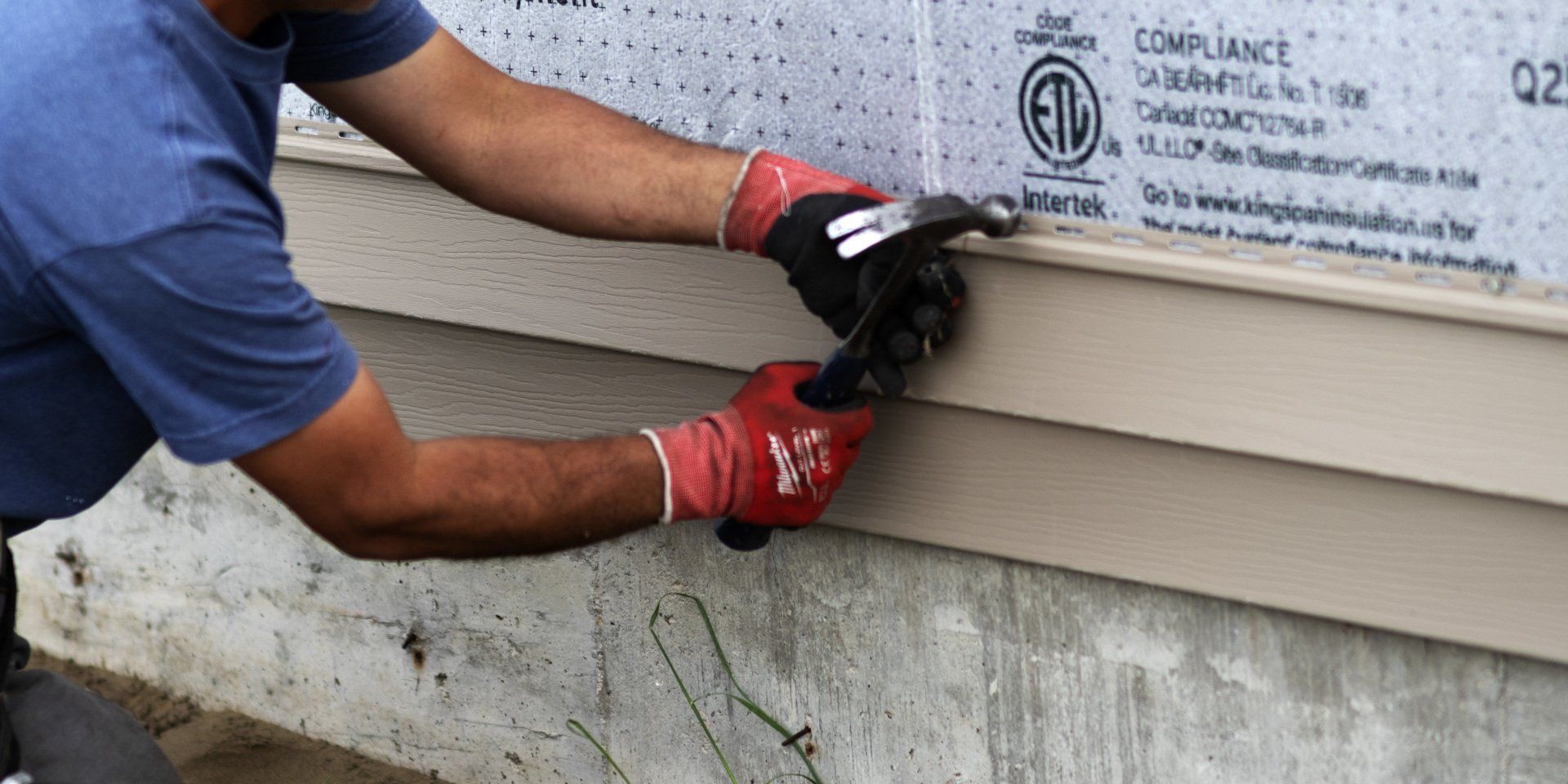 a man wearing red gloves is installing siding on a house .