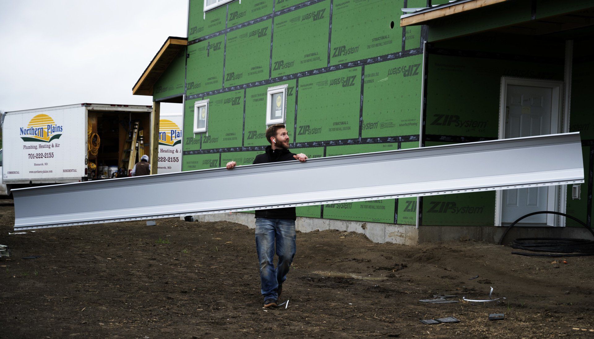 a man is carrying a large piece of metal in front of a house under construction .