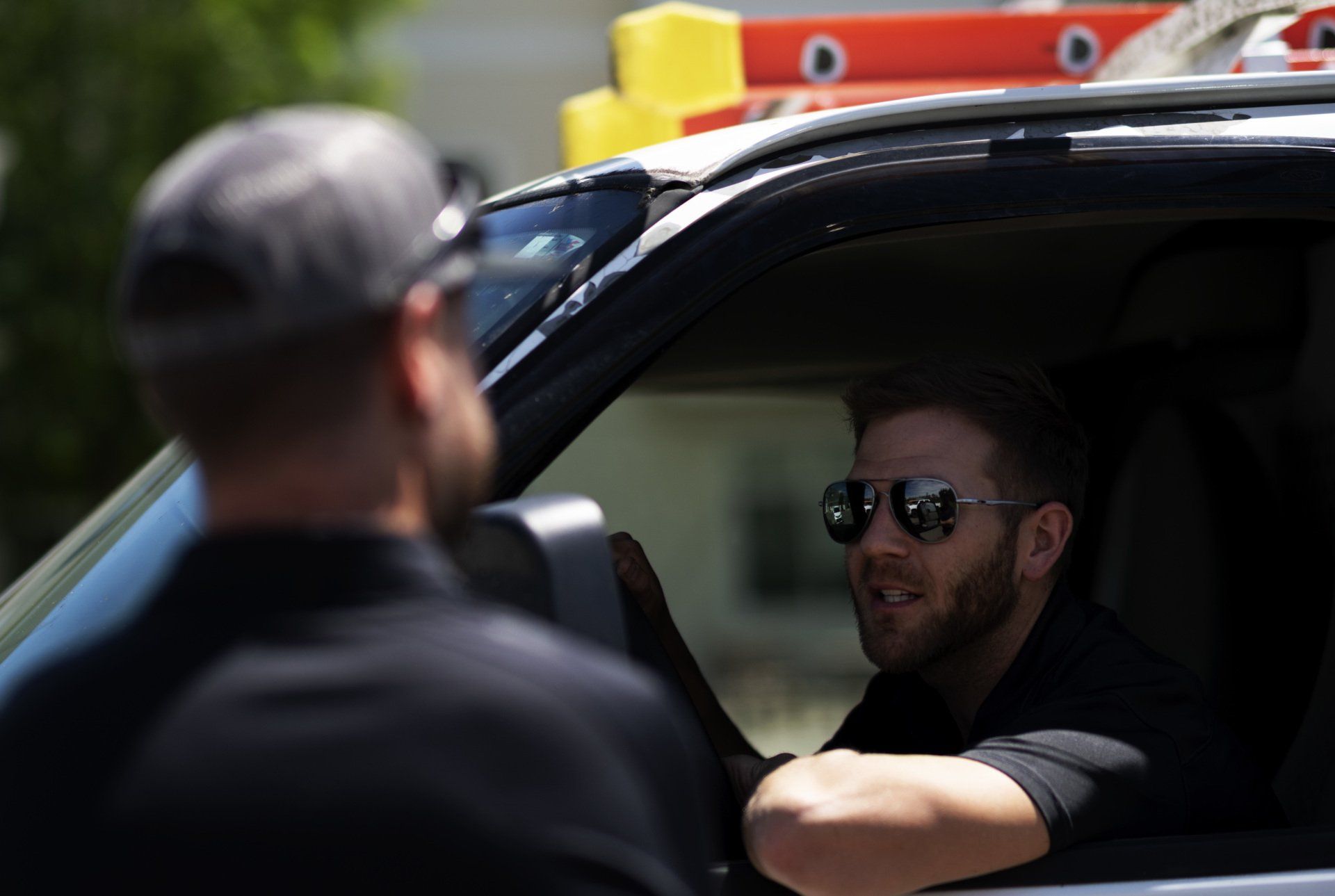 a man wearing sunglasses is sitting in the driver 's seat of a truck talking to another man .