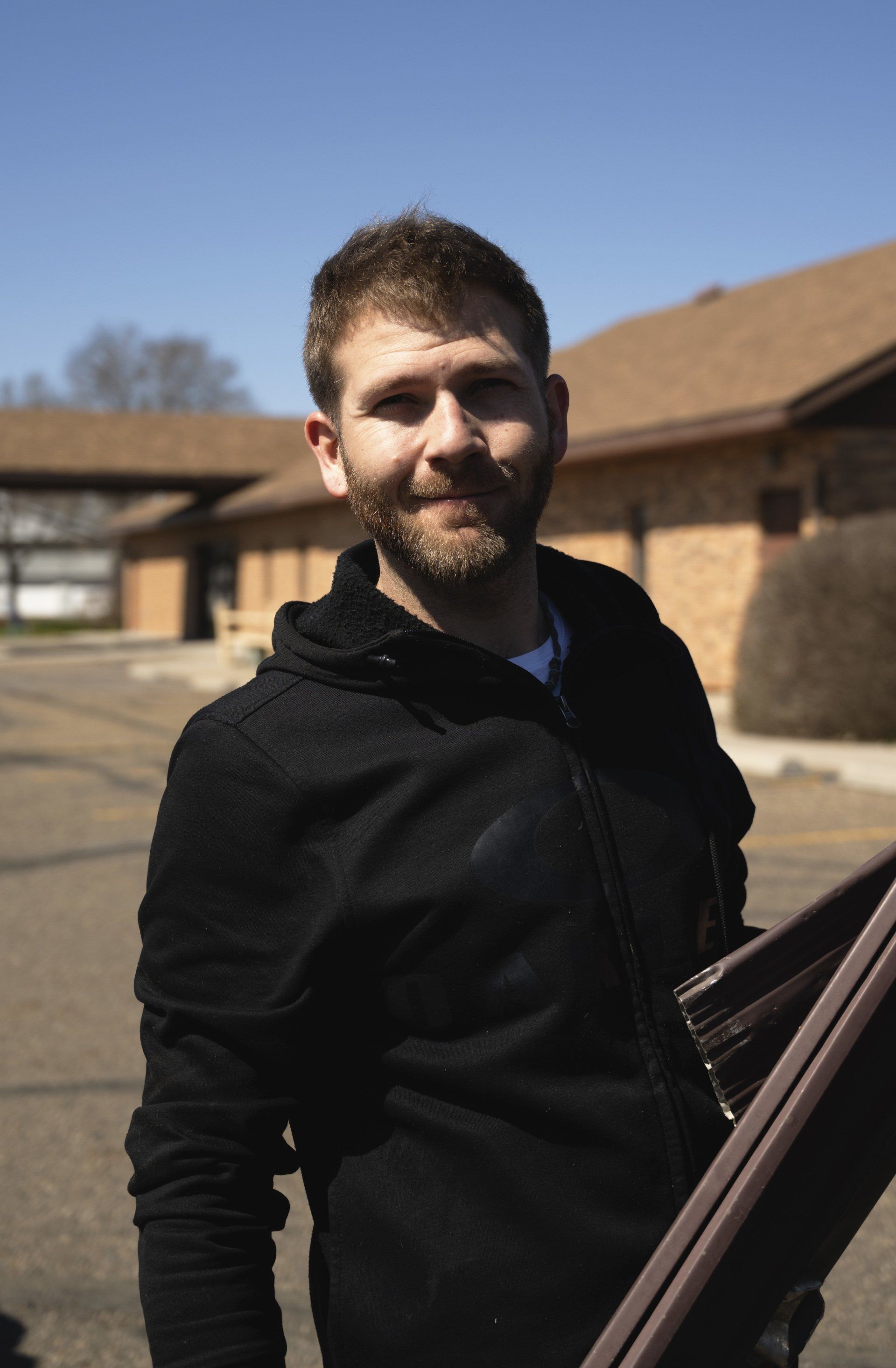 a man in a black jacket is holding a piece of wood in front of a building .
