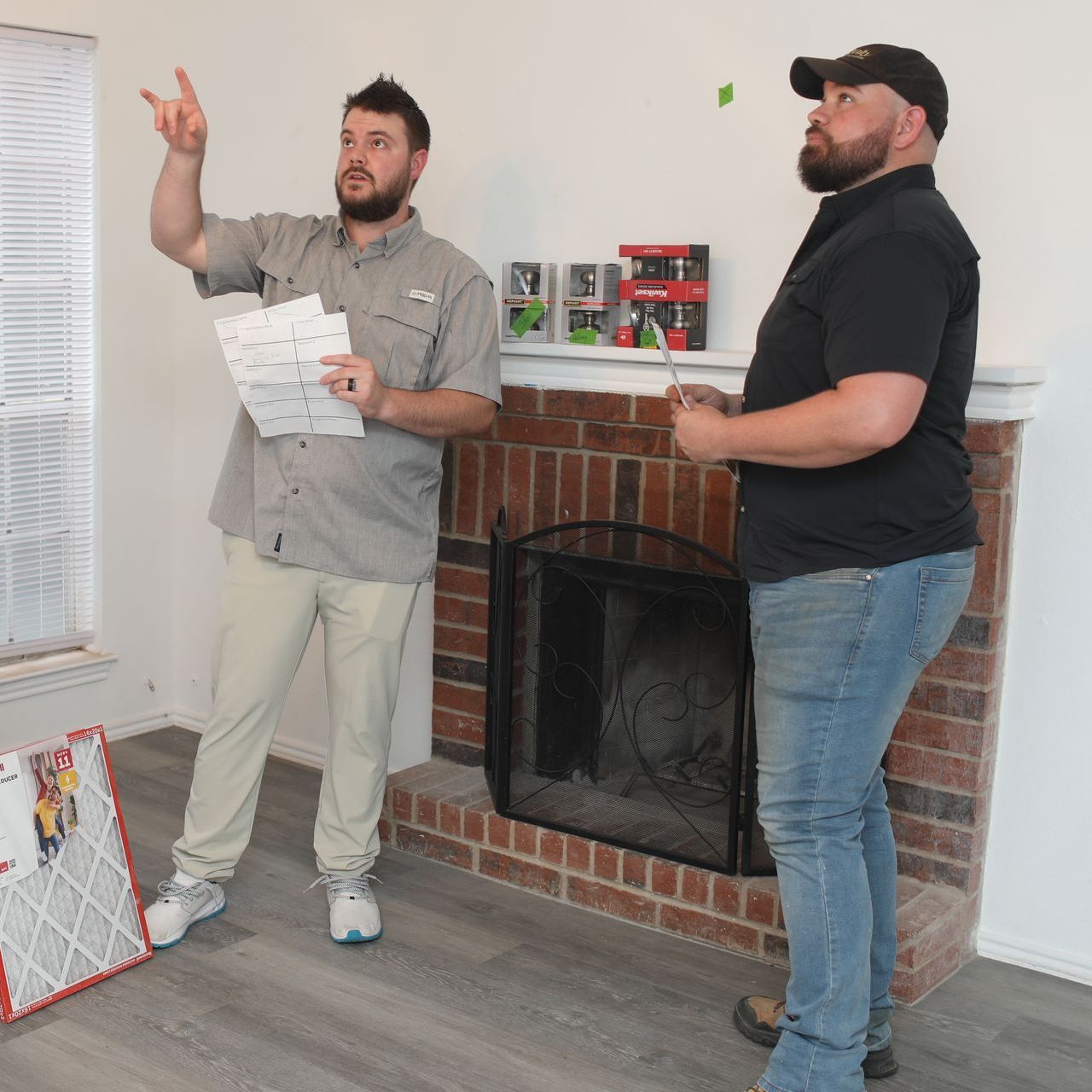 Two men are standing in a living room next to a fireplace.