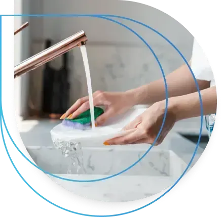 Person washing a white plate in a marble sink with a green sponge under running water. Person washing a white plate in a marble sink with a green sponge under running water.