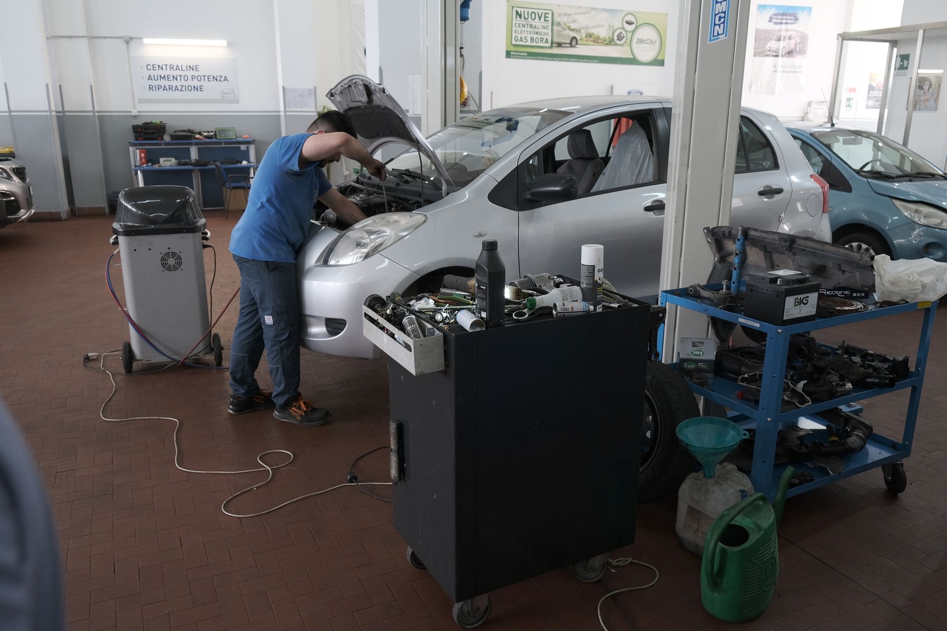 Meccanico al lavoro su un'auto argentata in un'officina. Attrezzi e attrezzature nelle vicinanze.