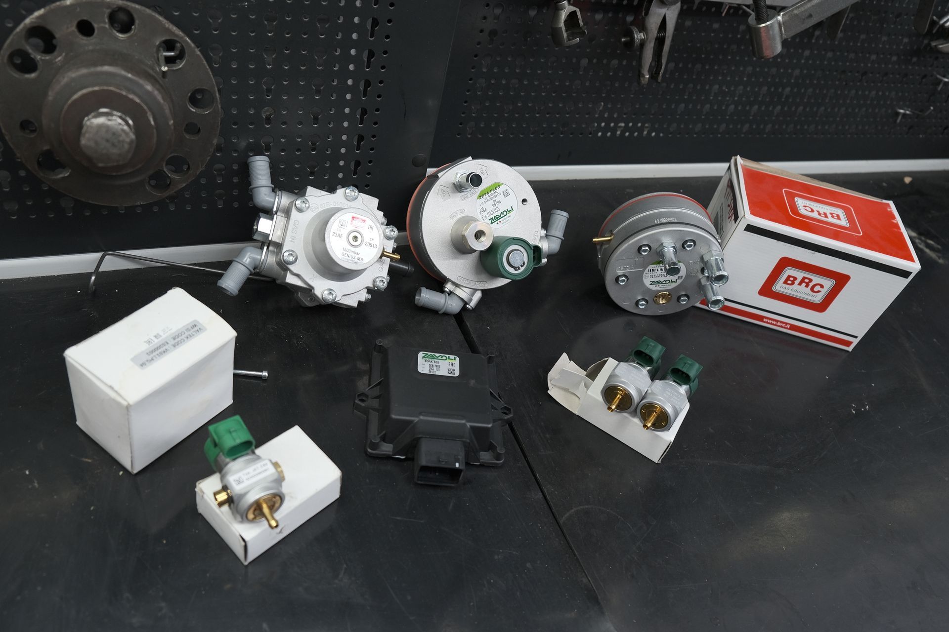 Vari pezzi di ricambio per automobili, per lo più bianchi e argentati, con una scatola rossa e bianca, su una superficie nera.