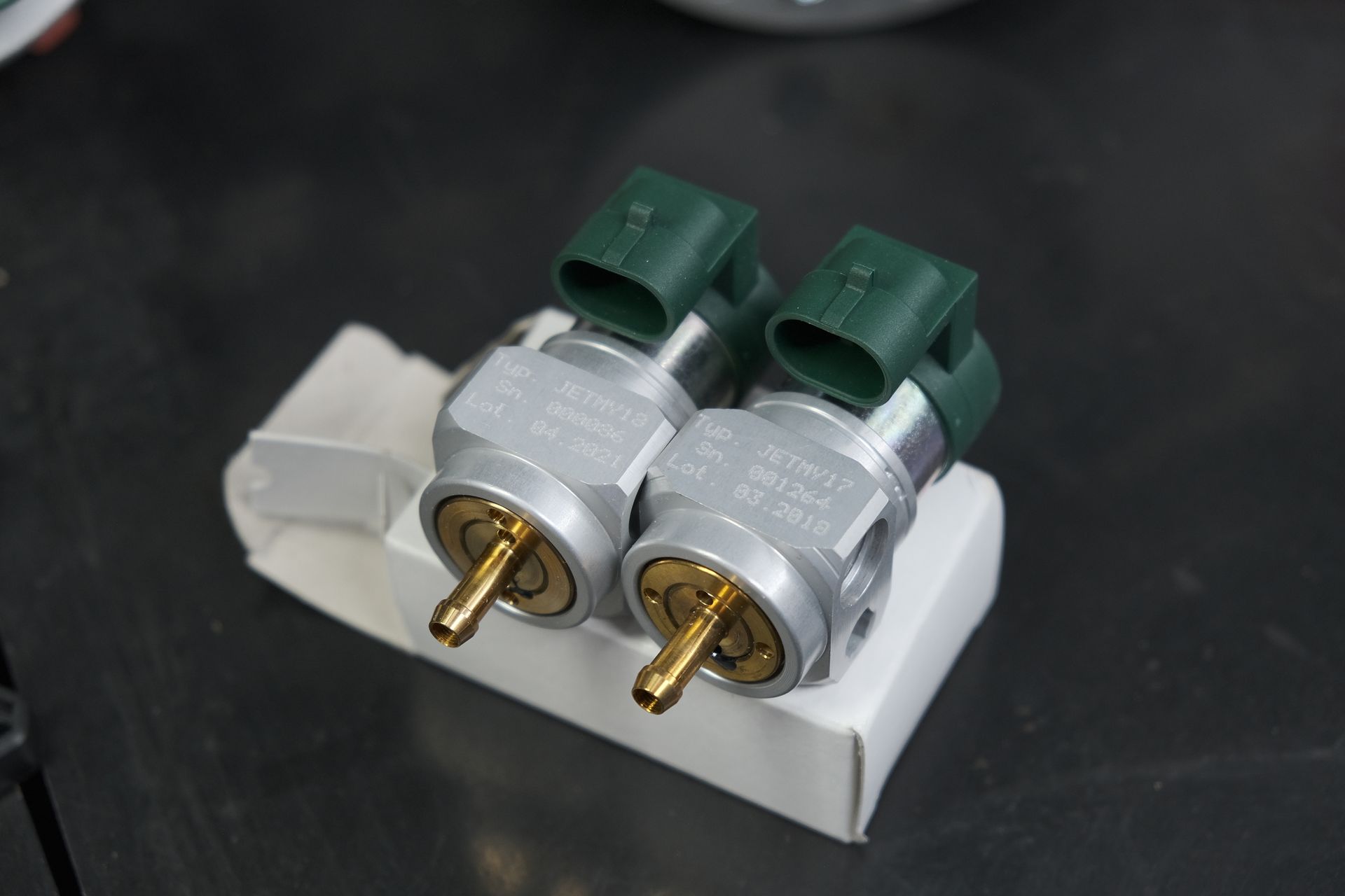 Due sensori argentati con connettori verdi, appoggiati su una scatola bianca, su una superficie scura.