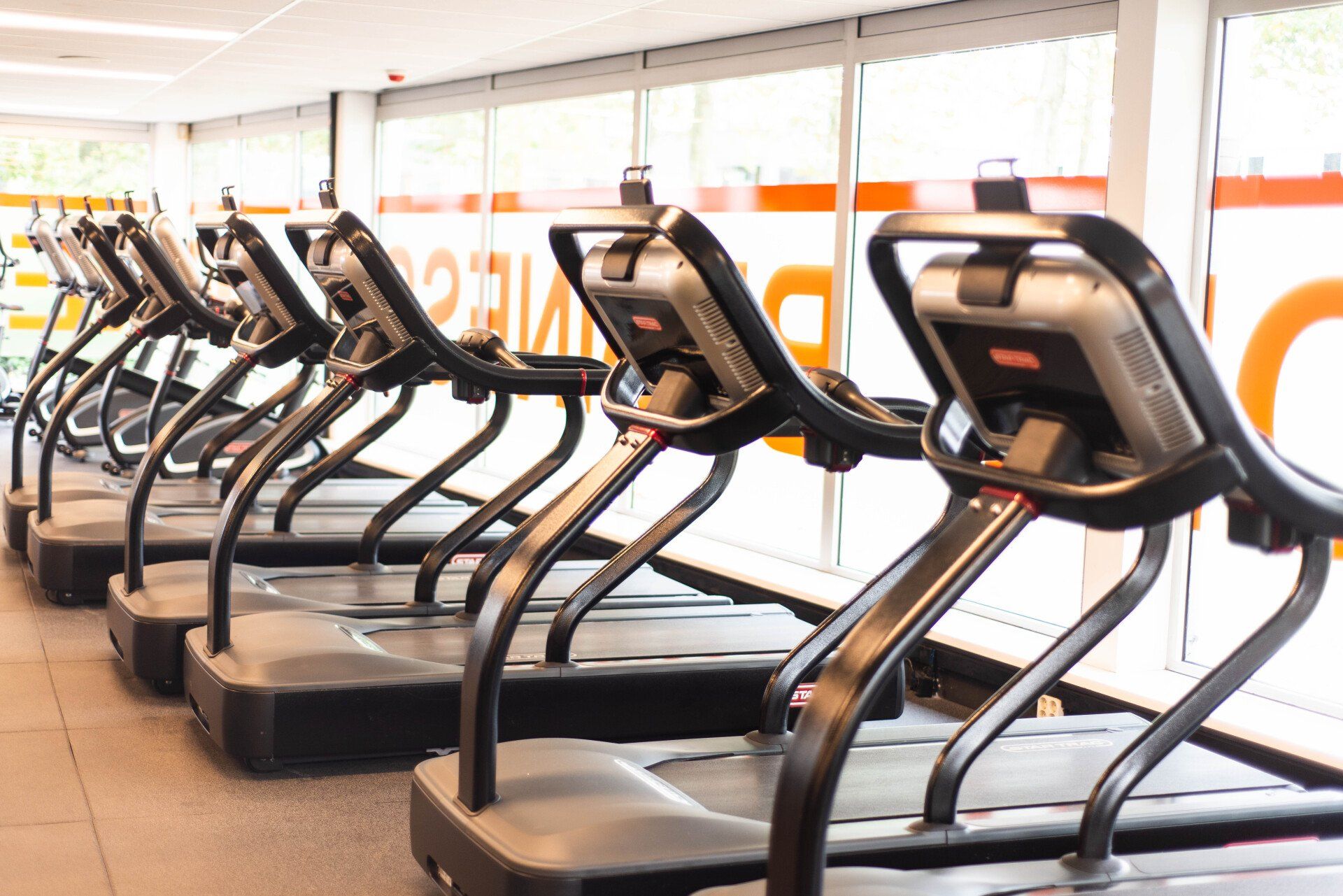 In een sportschool staat een rij loopbanden opgesteld.