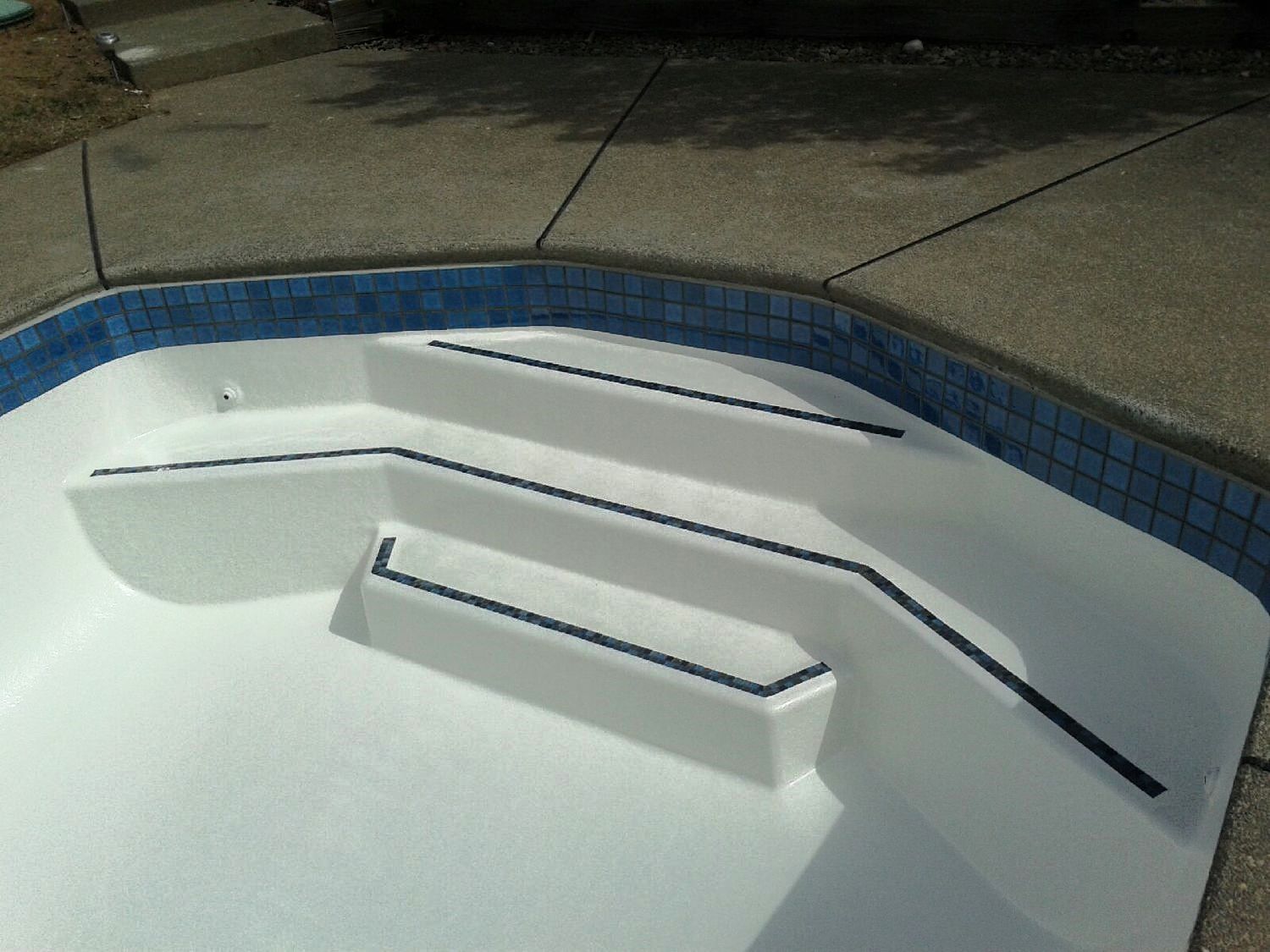 Pool steps painted white with dark handrails, blue tile trim, and gray concrete surround.