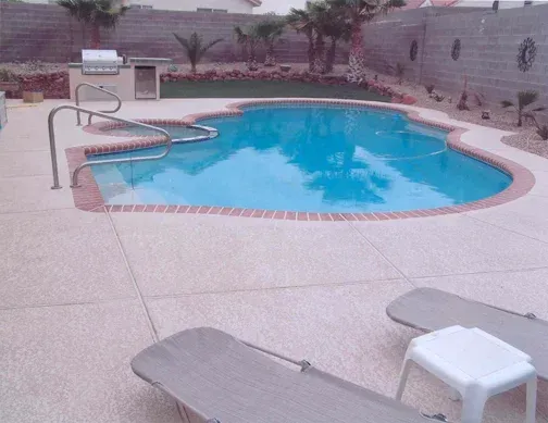 Swimming pool with brick border, patio, lounge chairs, and an outdoor kitchen.
