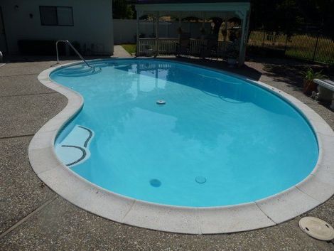 Blue swimming pool with a curved shape, surrounded by a concrete patio.