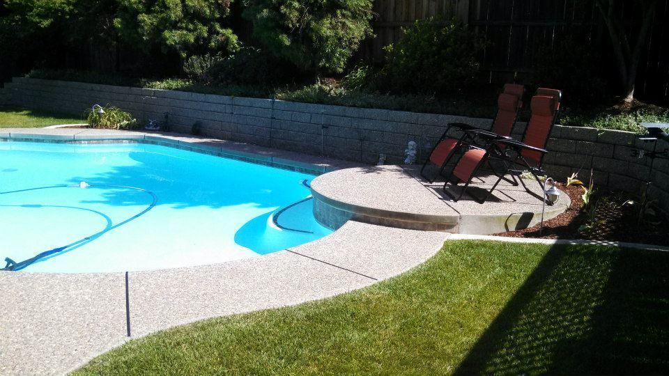 Poolside patio with lounge chairs, blue water, and green lawn. Poolside patio with lounge chairs, blue water, and green lawn.