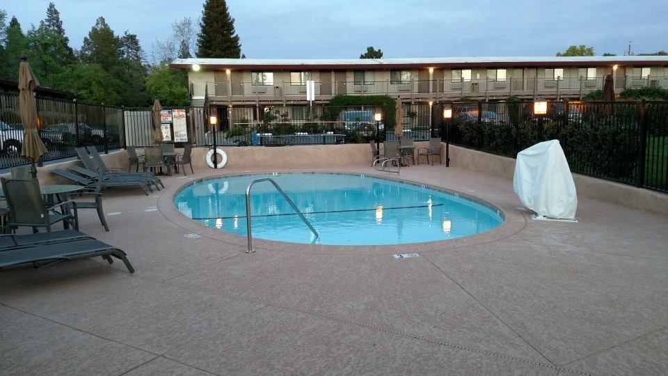 Pool area at a motel with lounge chairs, a covered hot tub, and the building in the background.