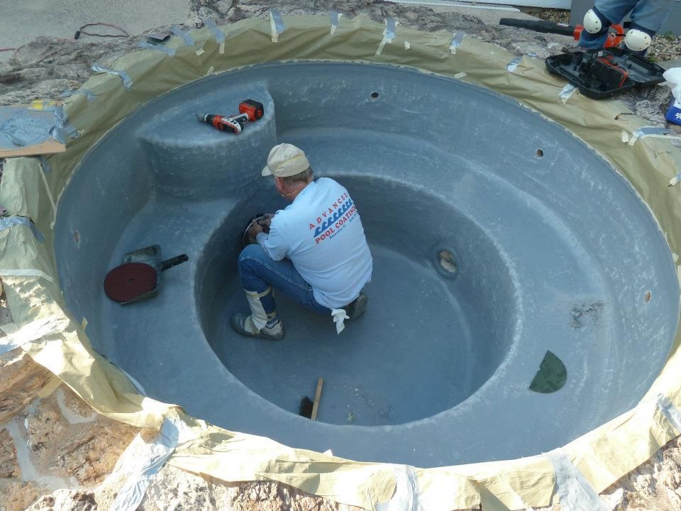 Person works on a gray, circular hot tub. Tools and beige tarp surround the tub in an outdoor setting.