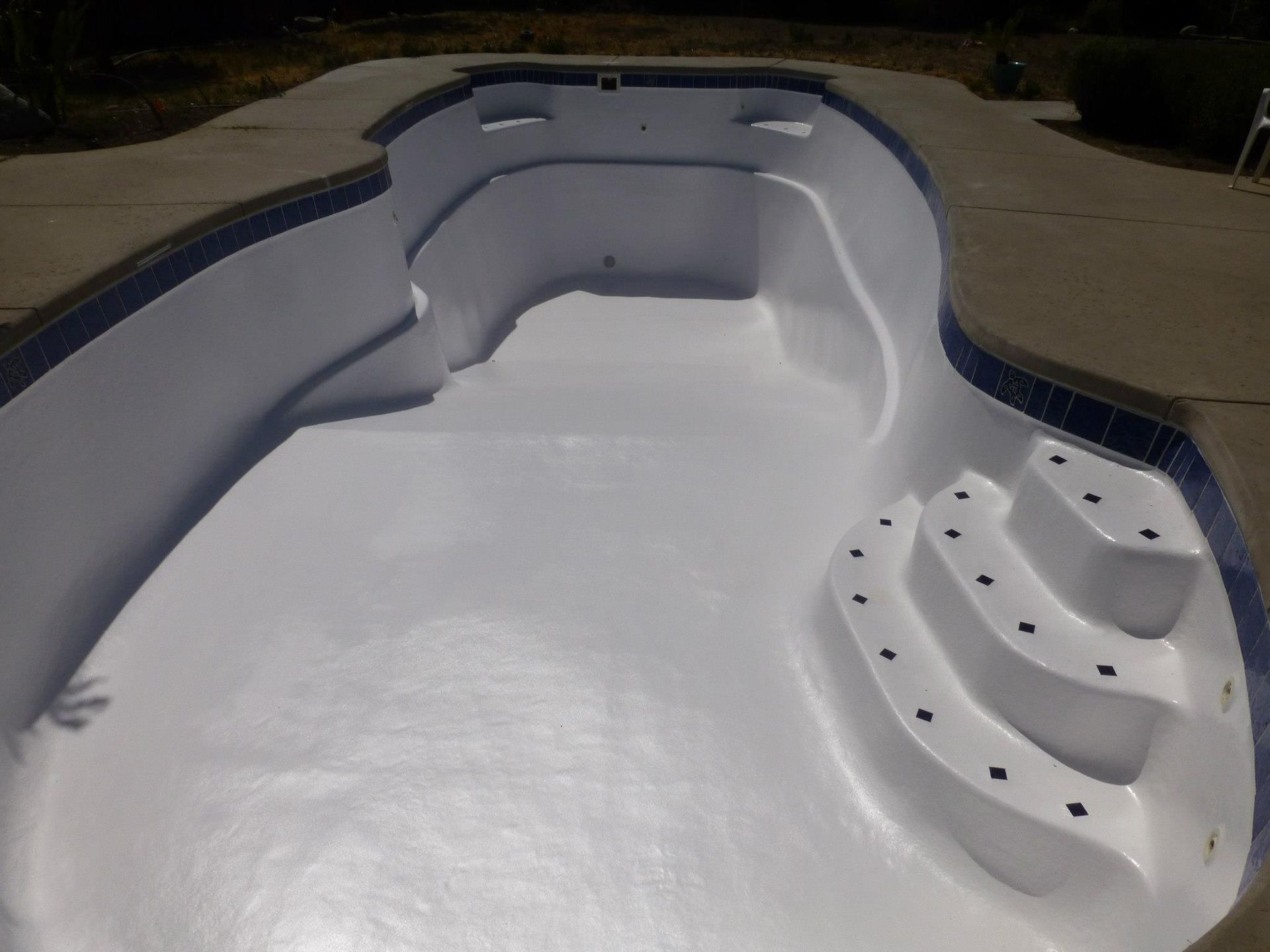 Empty swimming pool with white interior, blue tile border, and concrete surround.