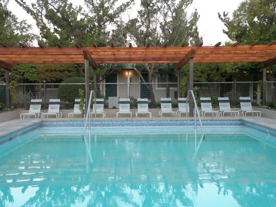 Swimming pool with lounge chairs under a wooden pergola; trees in the background.
