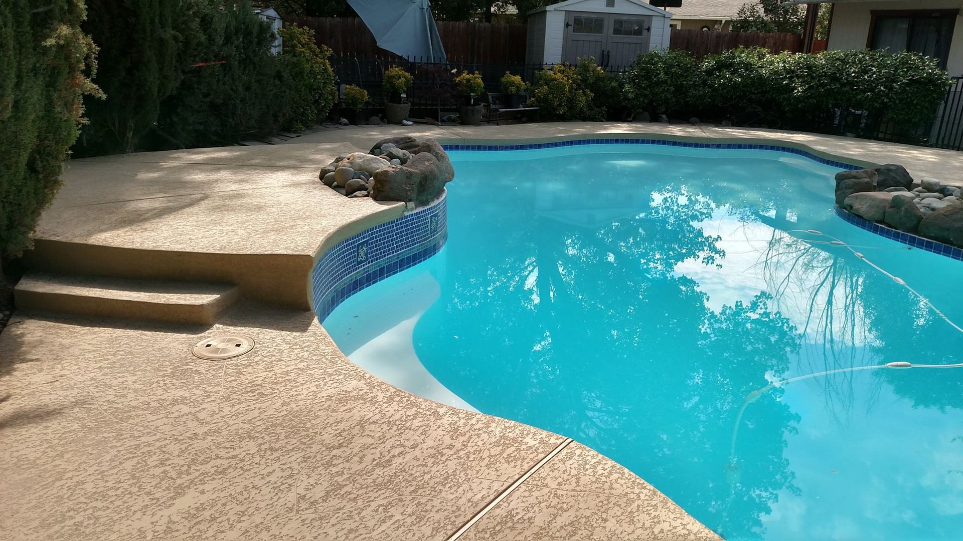 Pool with blue water and tan concrete surround; steps and rock accents. Pool with blue water and tan concrete surround; steps and rock accents.