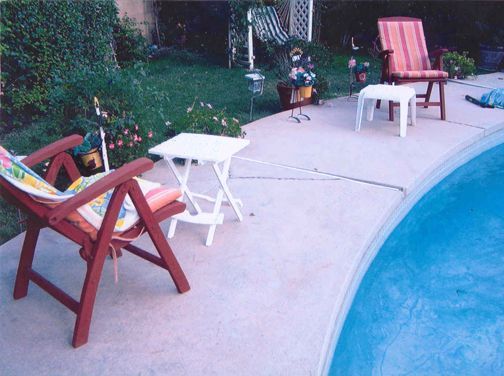 Poolside scene with chairs and small tables on a concrete deck, overlooking a swimming pool and grass. Poolside scene with chairs and small tables on a concrete deck, overlooking a swimming pool and grass.