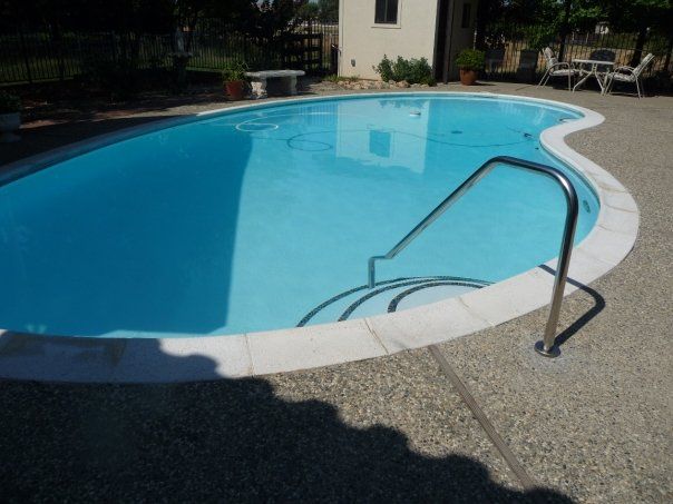 Pool with curved edges, blue water, stainless steel ladder, white coping, and concrete patio.
