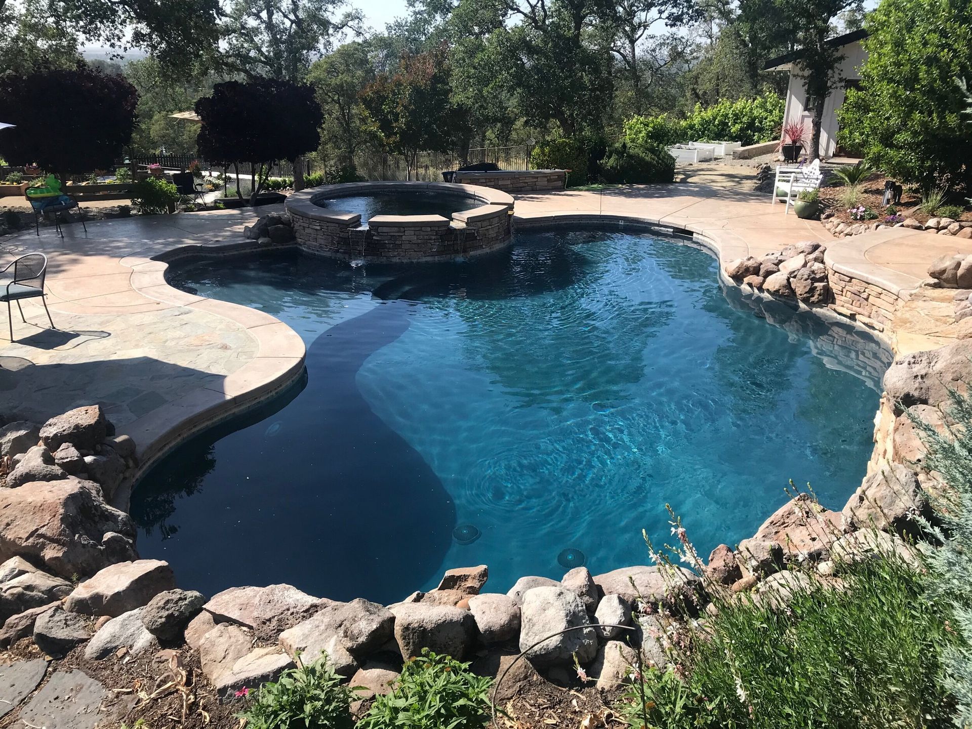 Pool with dark blue water and a built-in hot tub, surrounded by stone and concrete patio.