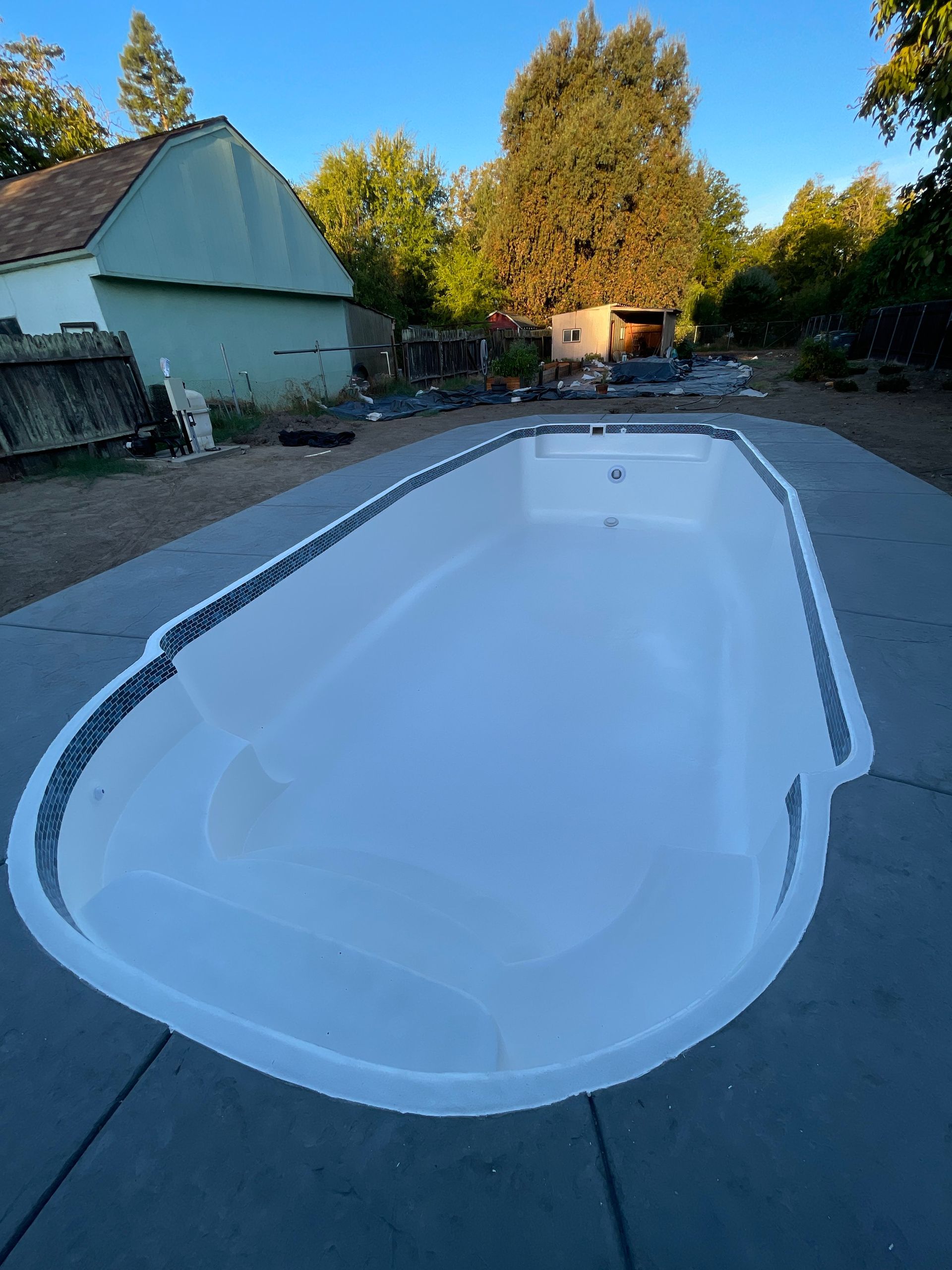 Empty white swimming pool, oval shape, set in concrete, outdoor setting.