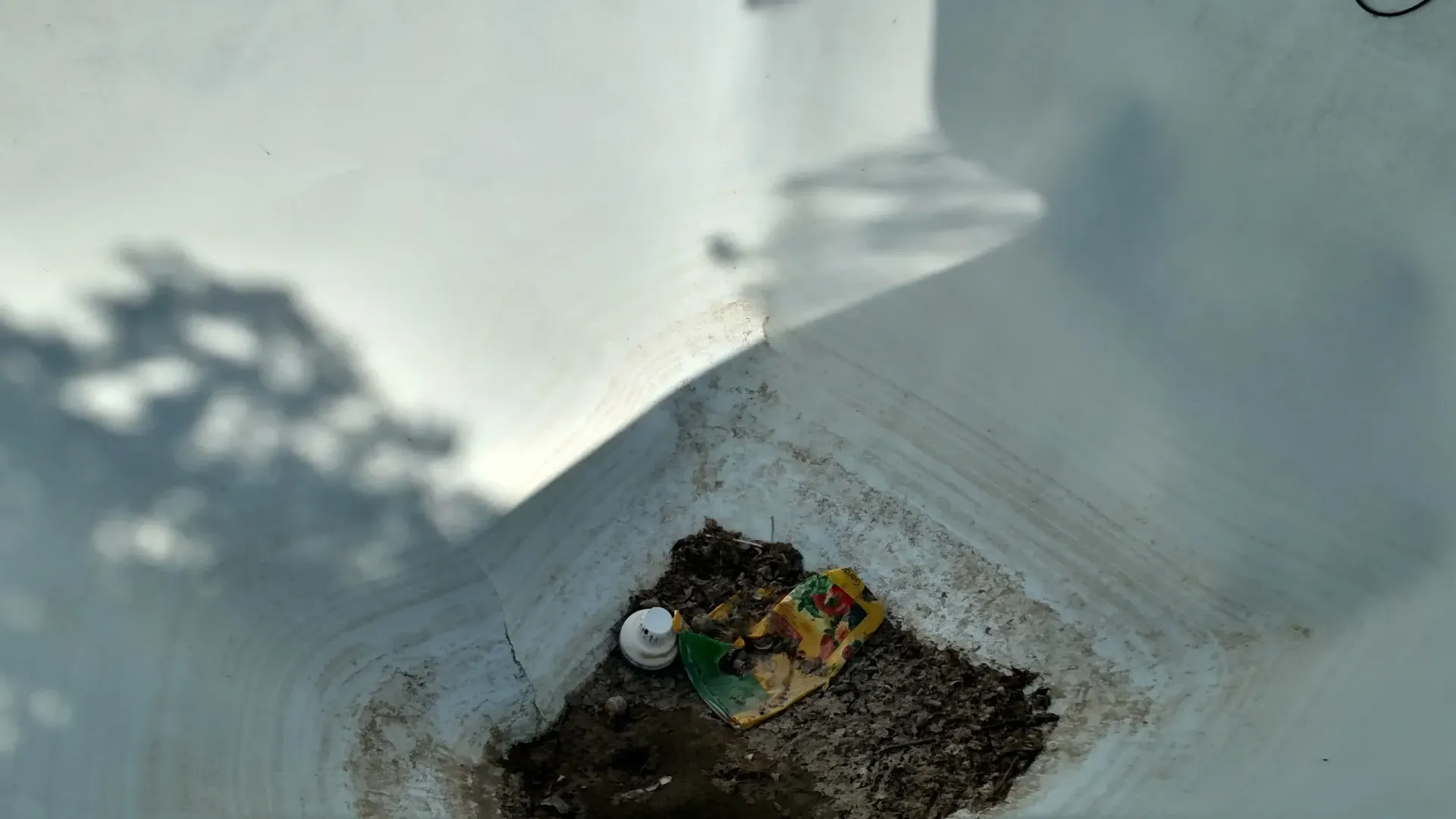 An overhead view of a white rectangular container with debris and shadows.