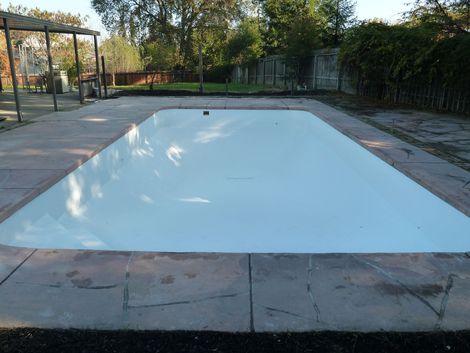 Rectangular pool covered with a white tarp, surrounded by concrete and grass, outdoors.