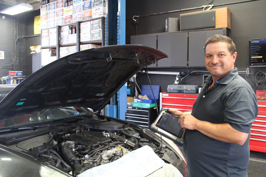Mechanic holding a tablet, inspecting a car engine in a repair shop.