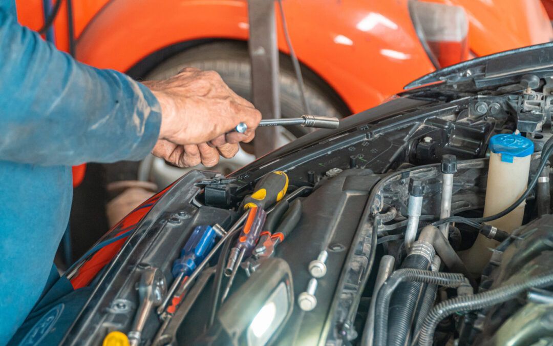 Mechanic using a wrench to work on a car engine. Tools are arranged on the car.
