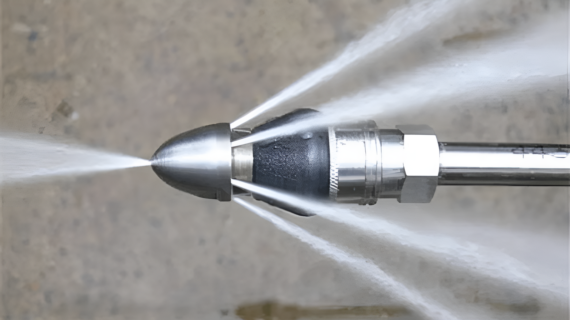 A drain cleaning nozzle spraying high-pressure water. Stainless steel nozzle with jets of water shooting out.