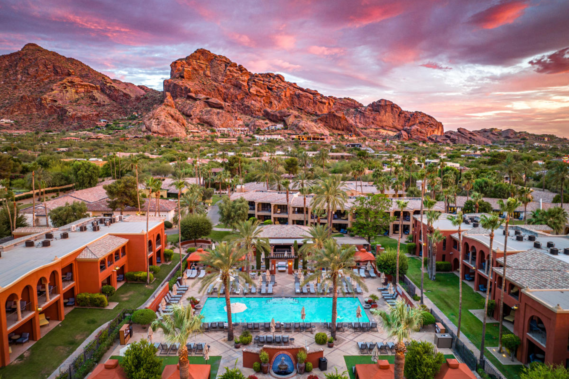 An aerial view of a resort with a large swimming pool and mountains in the background.