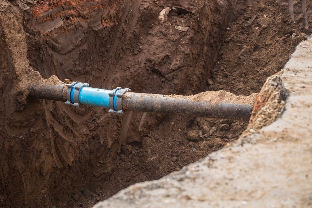 Blue pipe section connected to a grey pipe in an open trench.