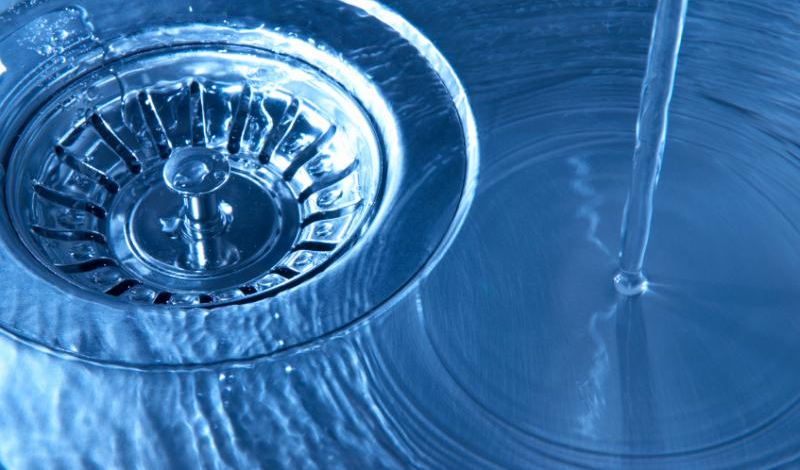 Water flowing into a stainless steel sink drain.