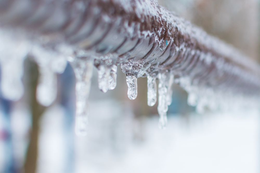 Icicles are hanging from a metal pipe in the snow.