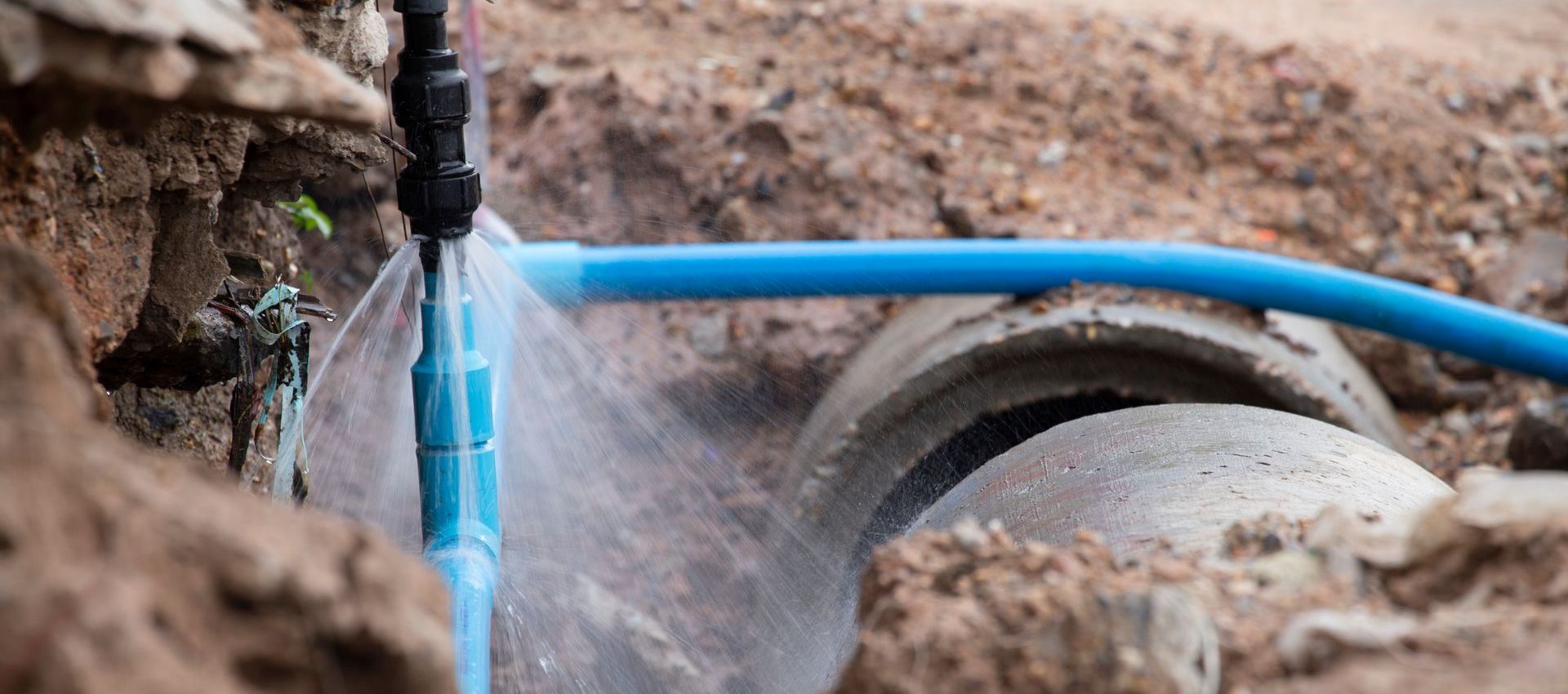 A blue hose is spraying water on a concrete pipe.
