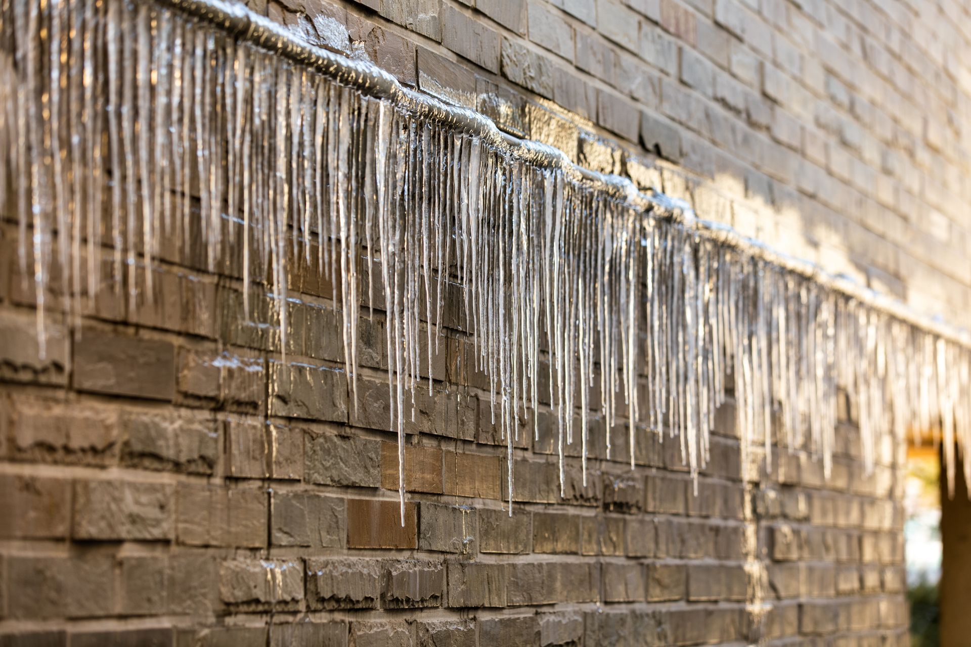 Icicles hanging from a brick building on a sunny day.