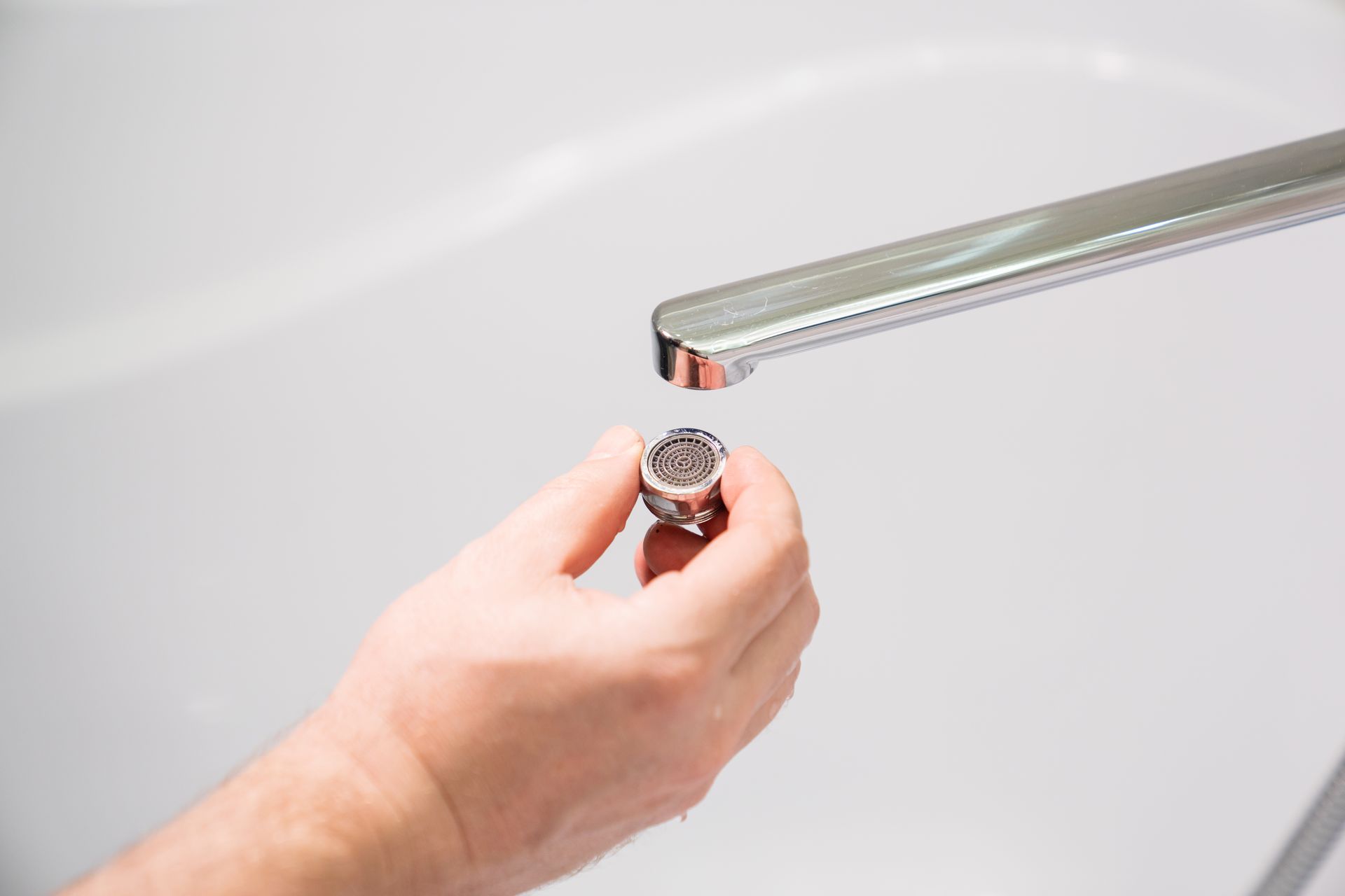 Hand holding a faucet aerator near a chrome faucet above a white bathtub.