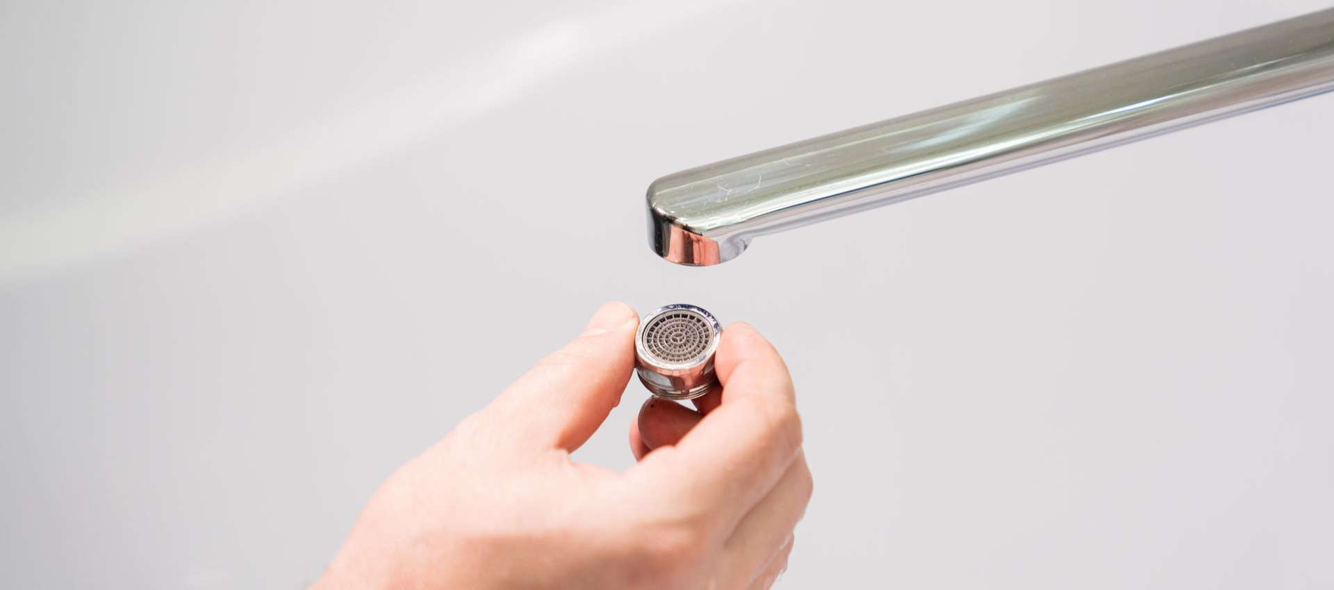 Hand holding a faucet aerator, ready to be attached to a shiny, silver faucet above a white sink.