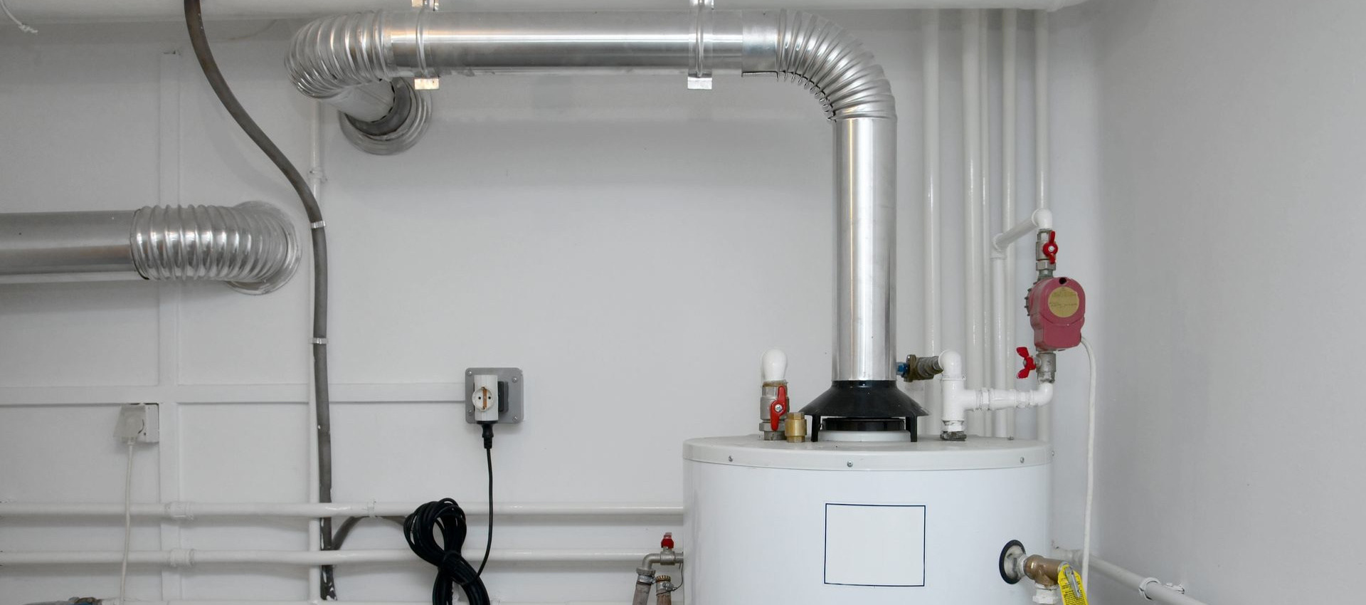 A utility room with a water heater, boiler, and pipes against tiled walls, next to an open doorway.