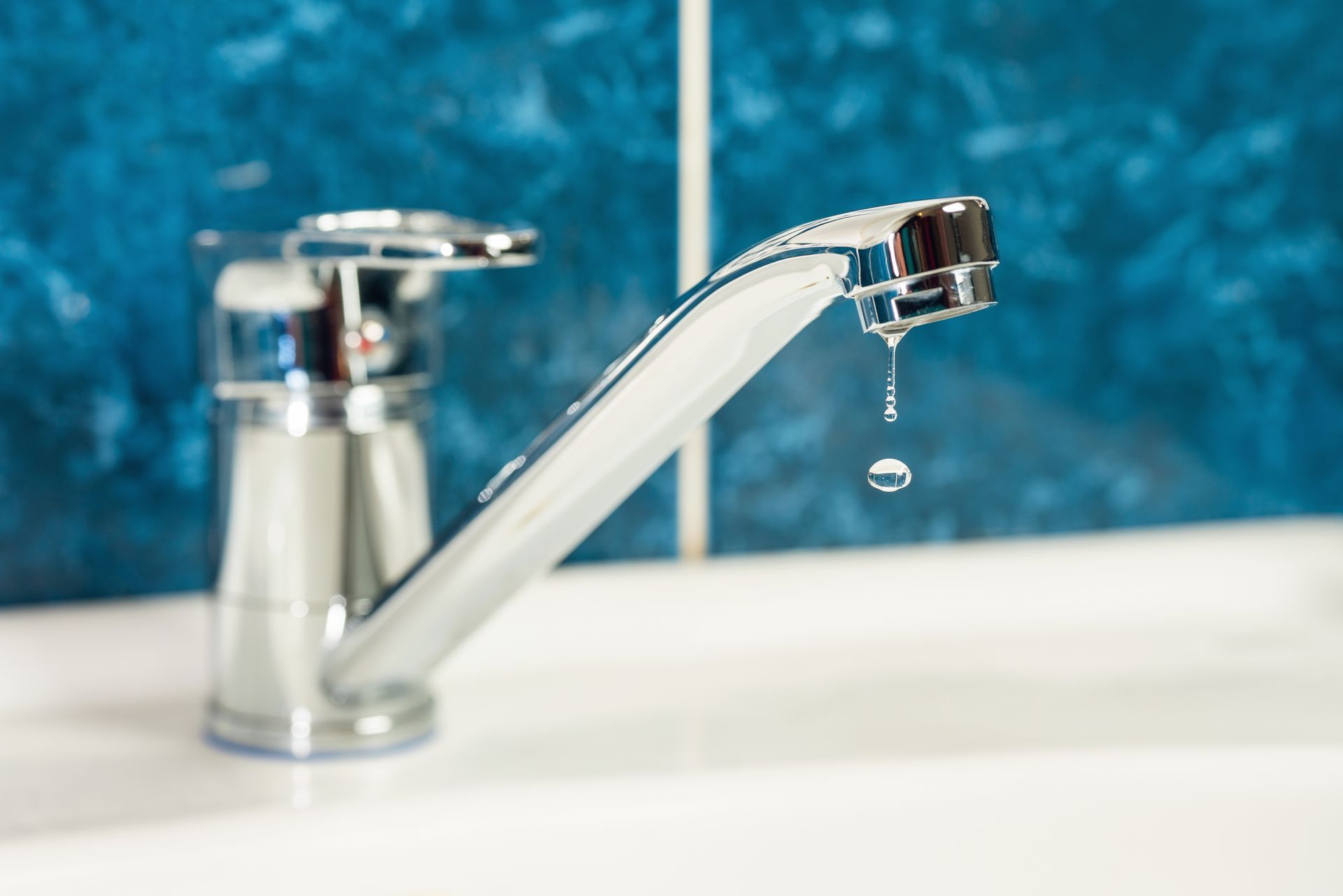 Chrome faucet with a dripping water drop against a blue-tiled wall.