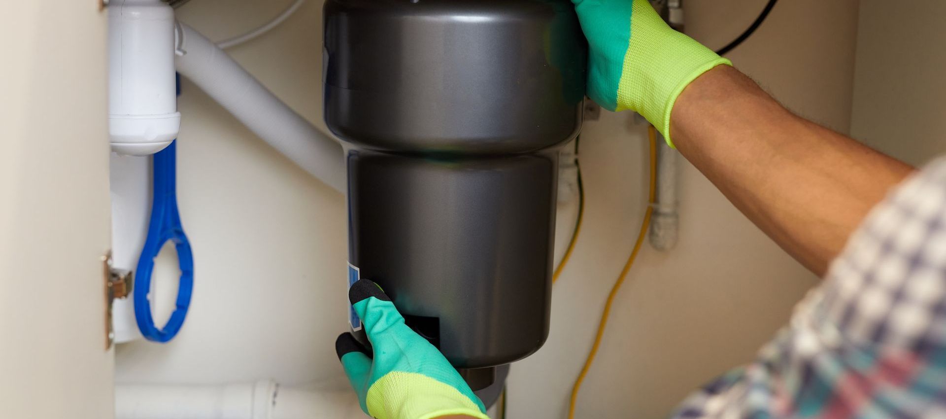 A person is fixing a garbage disposal under a sink.