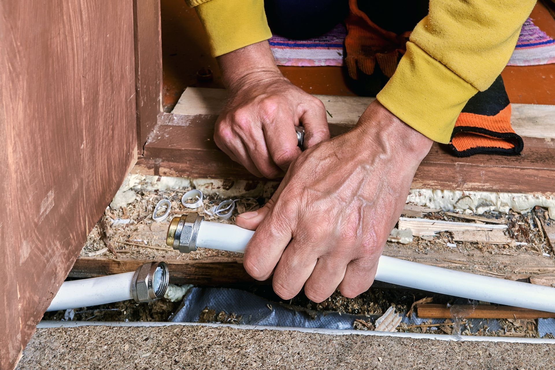 Hands connecting white pipe, possibly for plumbing, in a wooden door frame.