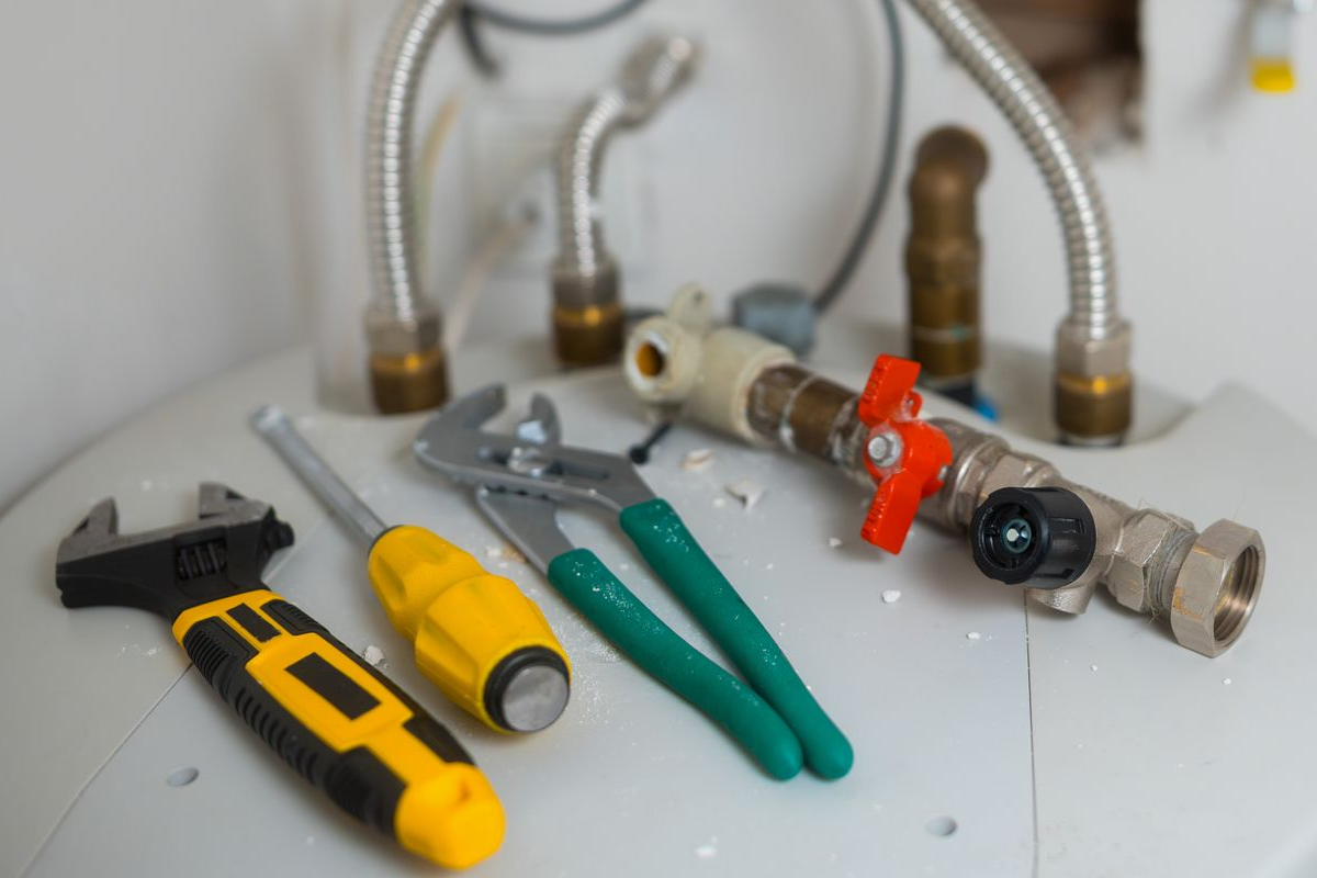 Tools on top of a water heater: wrench, screwdriver, pliers, pipes, and valve.