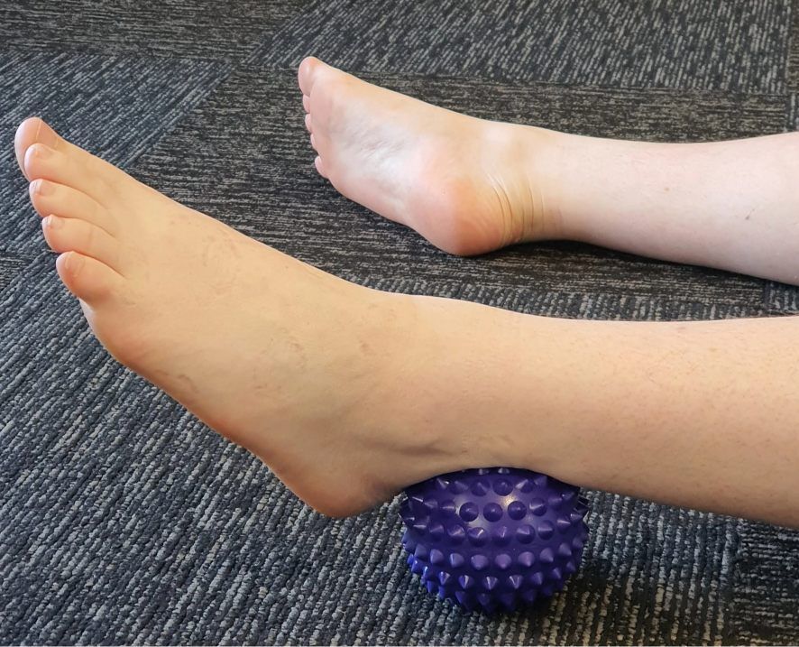 A Person is Laying on the Floor With Their Foot on a Purple Massage Ball — Anderson Family Chiropractic Health Centre in Mount Pleasant, QLD
